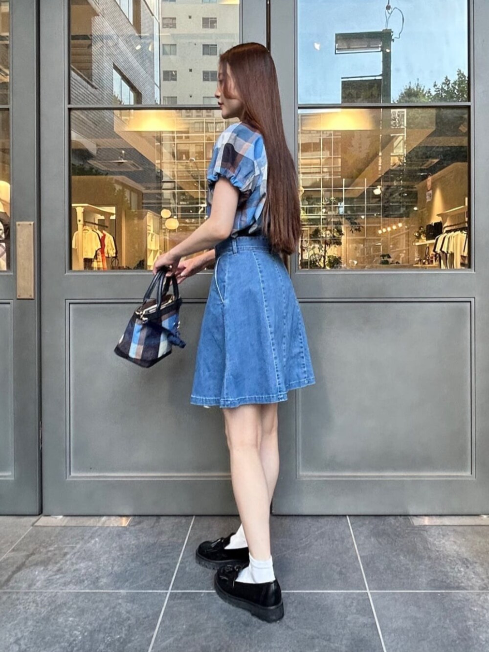 ブラック系のローファー、ブルー系のショルダーバッグ、ブルー系のデニムスカートを着用したレディースの夏コーディネートの2枚目の写真