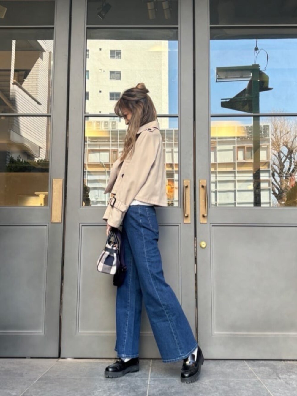 ベージュ系のショルダーバッグ、ベージュ系のトレンチコート、ブルー系のデニムパンツを着用したレディースの秋コーディネートの2枚目の写真