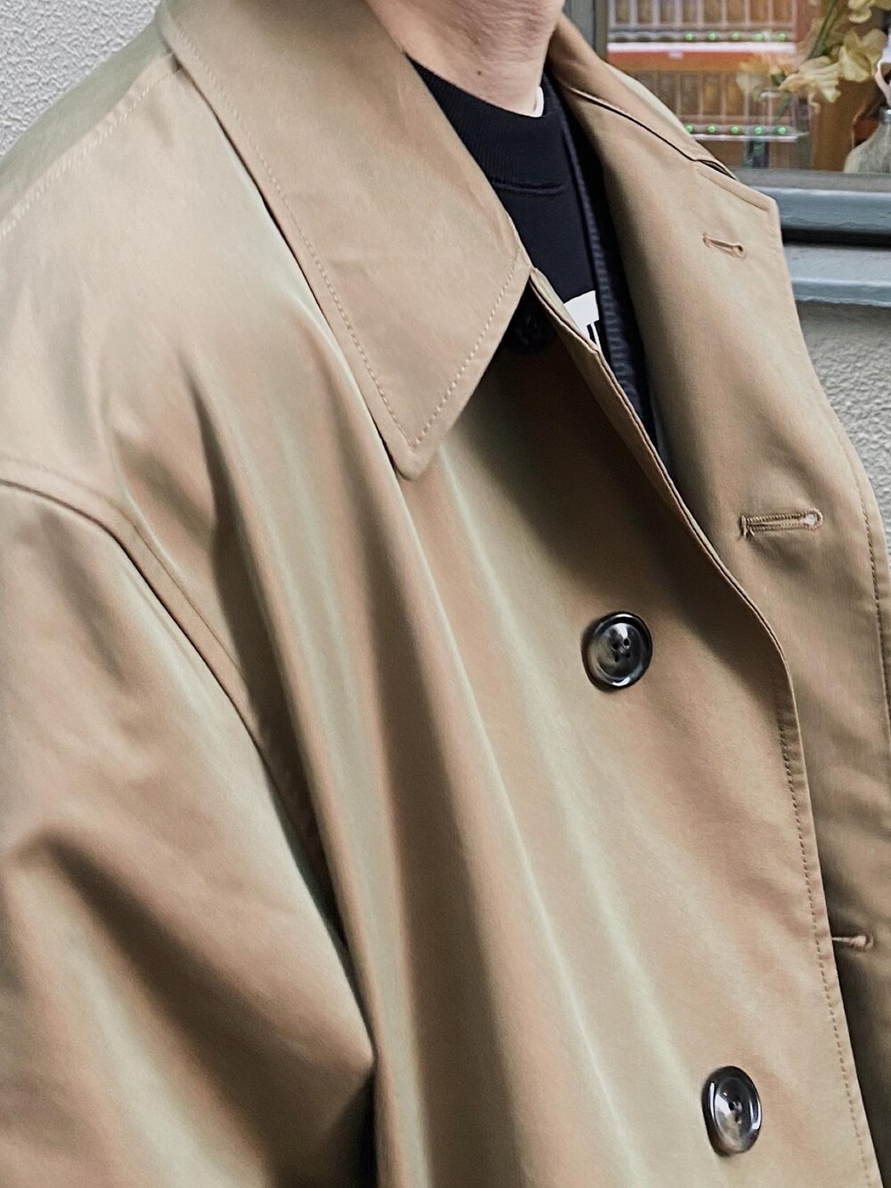 ブラック系のスウェット、ベージュ系のステンカラーコート、グレー系のスラックスを着用したメンズの春コーディネートの2枚目の写真