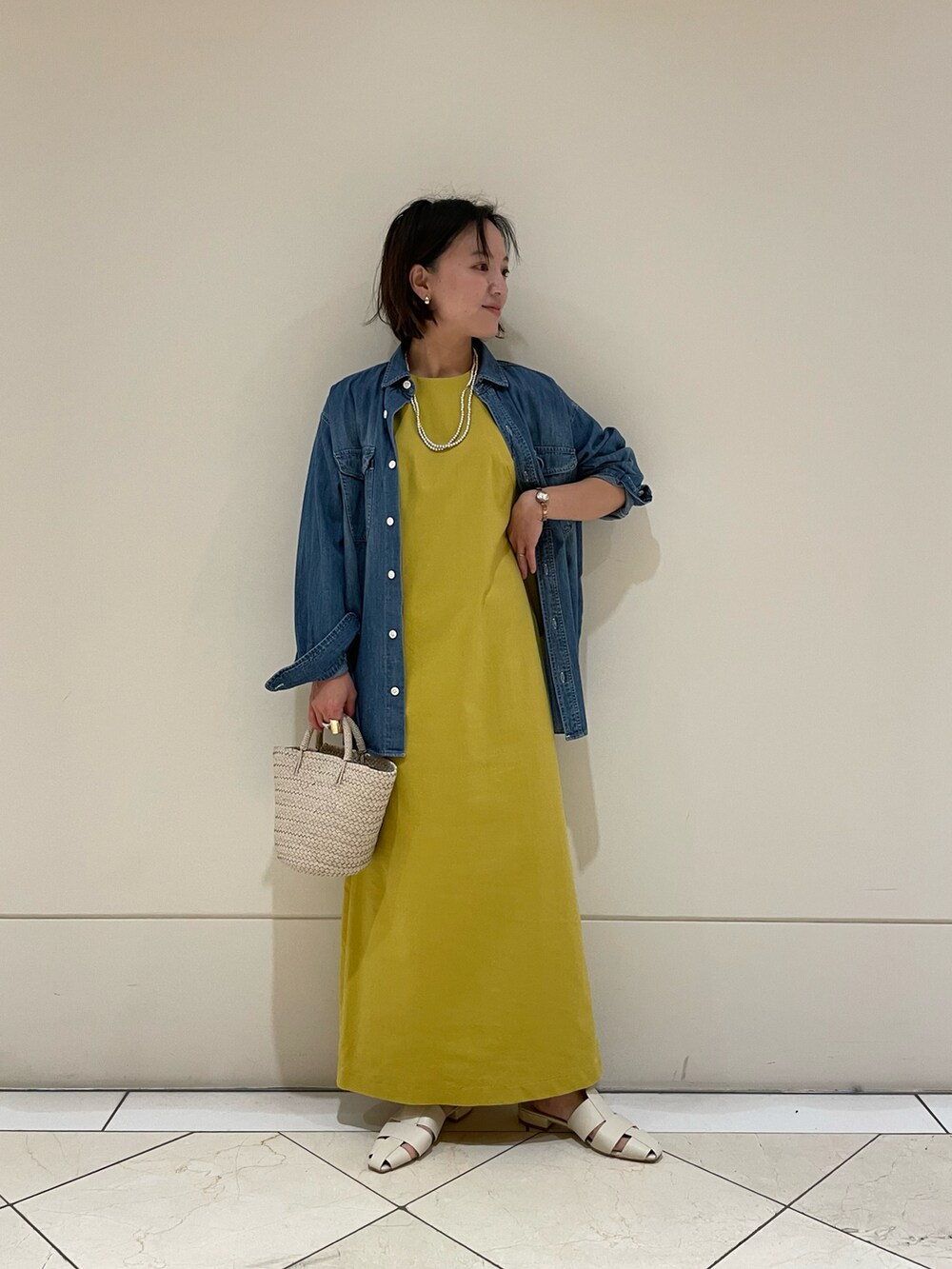 イエロー系のワンピース、ホワイト系のサンダル、ホワイト系のバッグを着用したレディースの春コーディネートの2枚目の写真