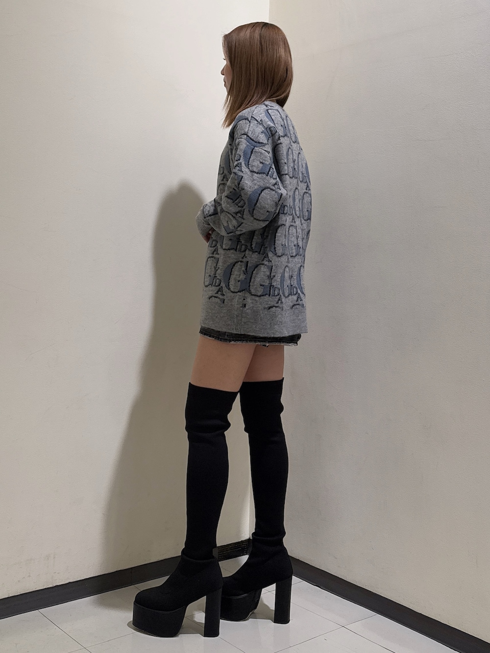 グレー系のニット/セーター、ブラック系のデニムスカート、ブラック系のブーツを着用したレディースの冬コーディネートの2枚目の写真