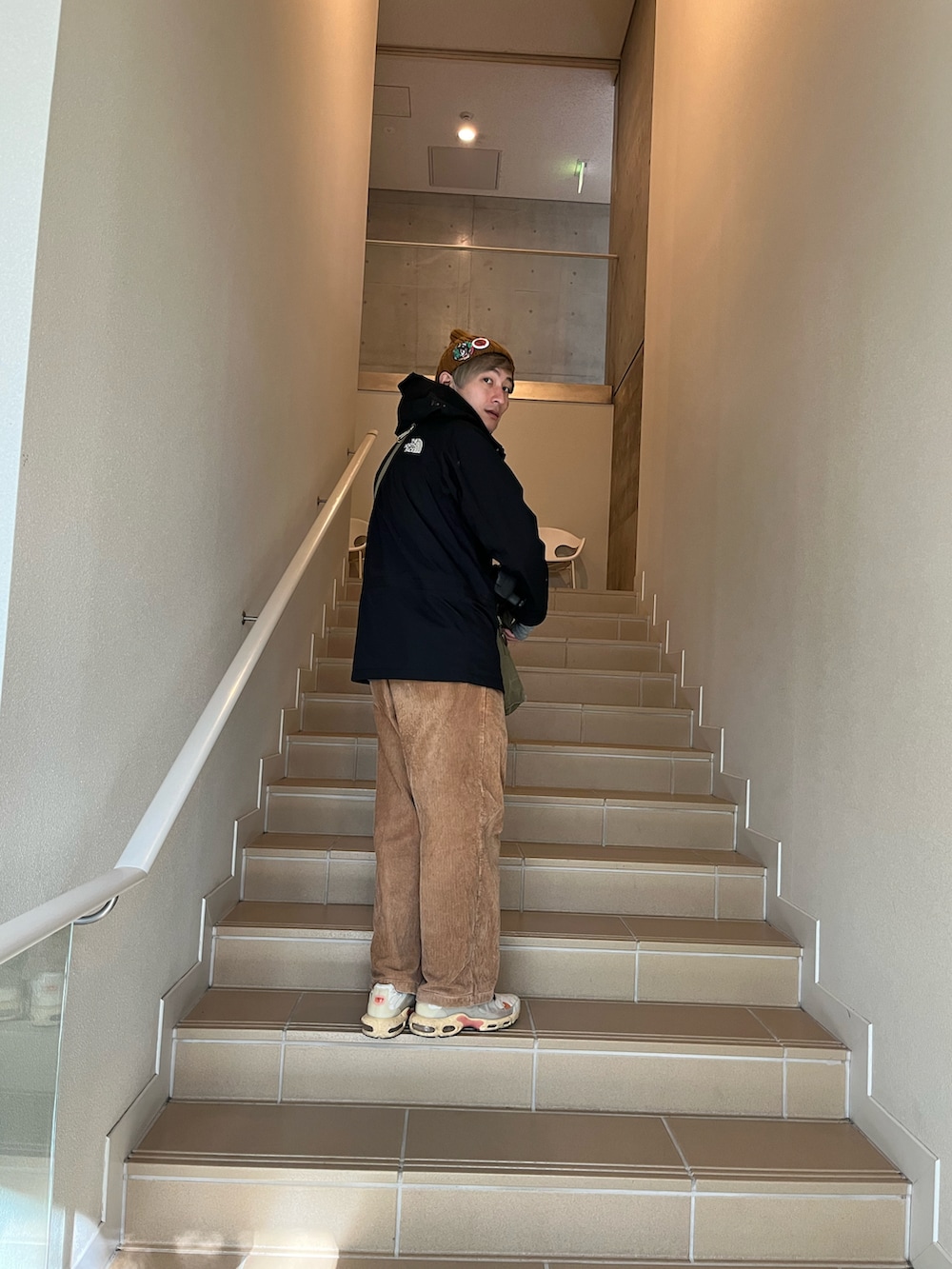 ベージュ系のスニーカー、ブラック系のマウンテンパーカー、グリーン系のショルダーバッグを着用したメンズの冬コーディネートの2枚目の写真