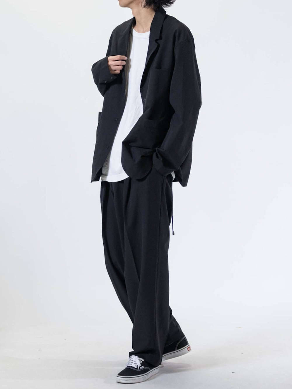 ブラック系のスニーカー、ブラック系のテーラードジャケット、ブラック系のチノパンツを着用したメンズの夏コーディネートの2枚目の写真