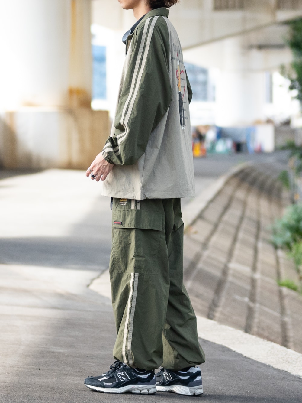 ブラック系のスニーカー、グリーン系のナイロンジャケット、グリーン系のカーゴパンツを着用したメンズの秋コーディネートの2枚目の写真