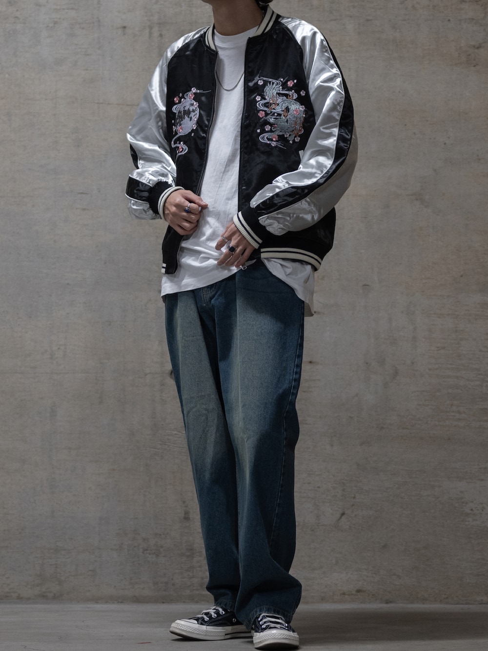 ブルー系のデニムパンツ、シルバー系のスカジャン、ブラック系のスニーカーを着用したメンズの秋コーディネートの2枚目の写真
