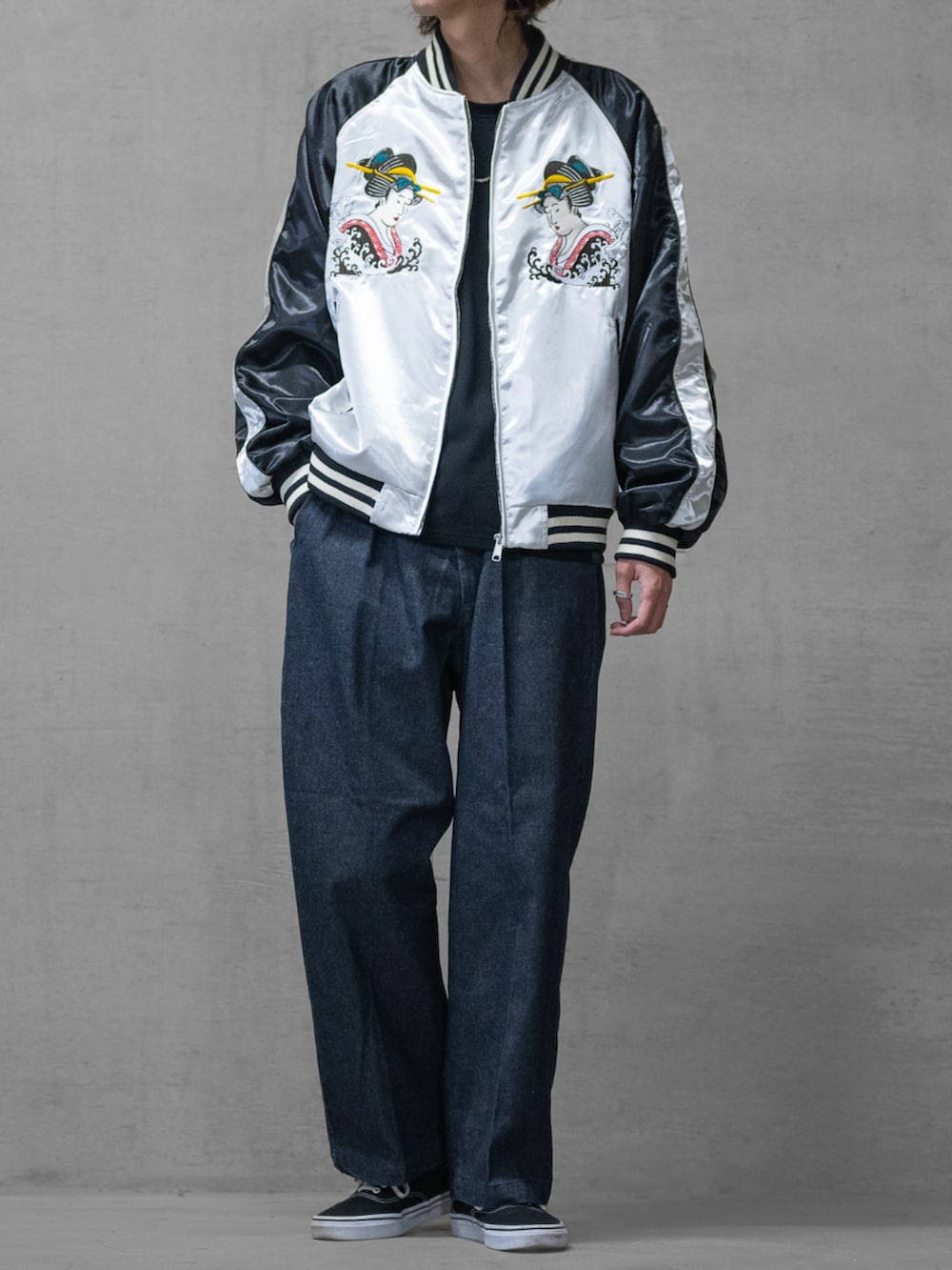 ブラック系のスニーカー、ブルー系のデニムパンツ、シルバー系のスカジャンを着用したメンズの春コーディネートの2枚目の写真