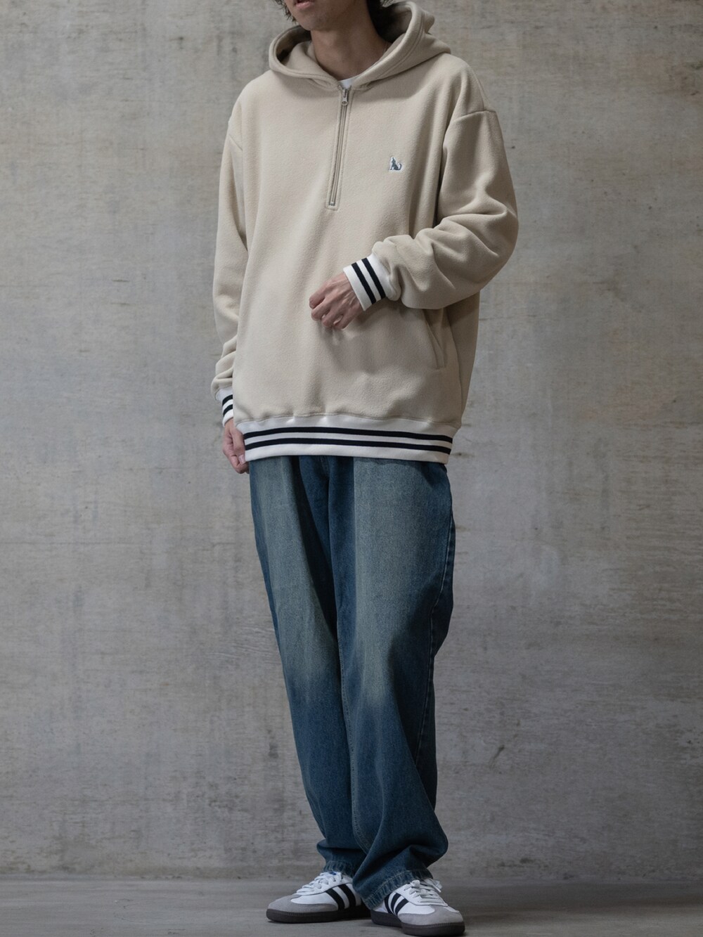 ブルー系のデニムパンツ、ホワイト系のスニーカー、ベージュ系のパーカーを着用したメンズの秋コーディネートの2枚目の写真