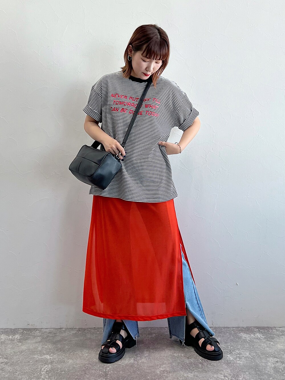 オレンジ系のワンピース、ブラック系のサンダル、ブラック系のTシャツ/カットソーを着用したレディースの夏コーディネートの2枚目の写真