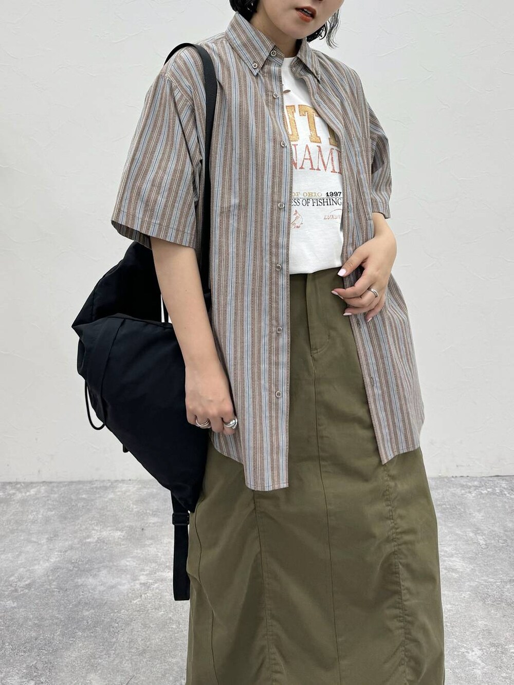 ブラック系のバックパック/リュック、グリーン系のスカート、ホワイト系のTシャツ/カットソーを着用したレディースの春コーディネートの5枚目の写真