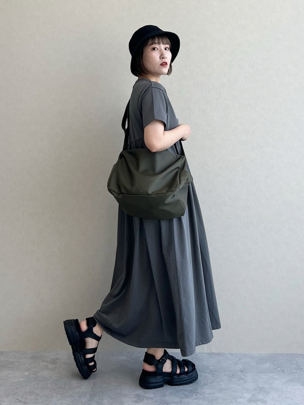グリーン系のショルダーバッグ、ブラック系のサンダル、グレー系のワンピースを着用したレディースの春コーディネートの2枚目の写真