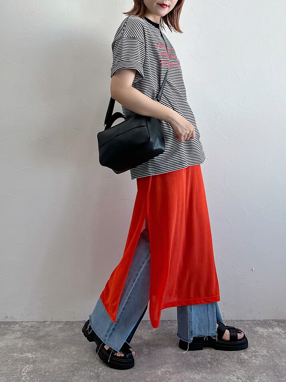 オレンジ系のワンピース、ブラック系のサンダル、ブラック系のTシャツ/カットソーを着用したレディースの夏コーディネートの5枚目の写真