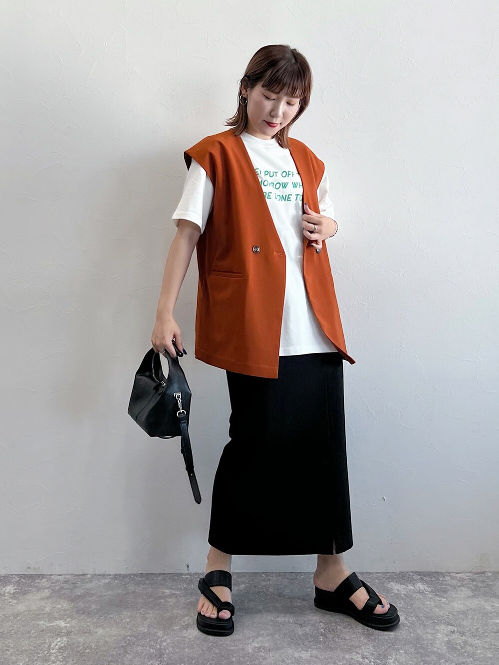 オレンジ系のワンピース、ブラック系のサンダル、ブラック系のTシャツ/カットソーを着用したレディースの夏コーディネートの4枚目の写真