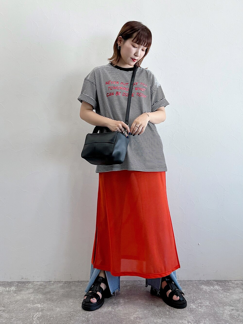 オレンジ系のワンピース、ブラック系のサンダル、ブラック系のTシャツ/カットソーを着用したレディースの夏コーディネートの3枚目の写真