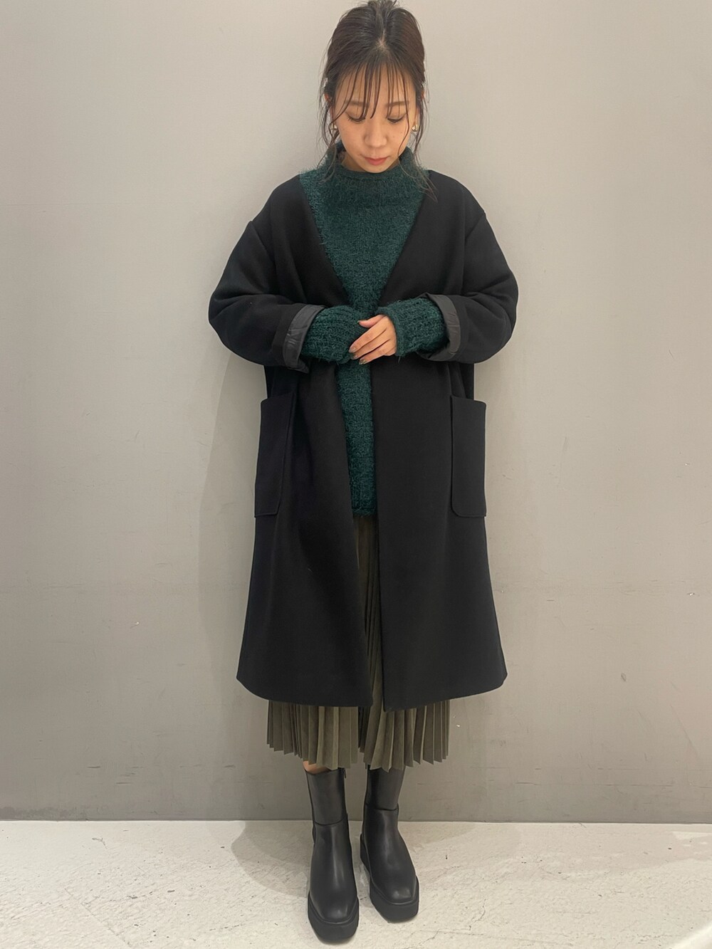 グレー系のスカート、グリーン系のニット/セーター、ブラック系のブーツを着用したレディースの冬コーディネートの2枚目の写真