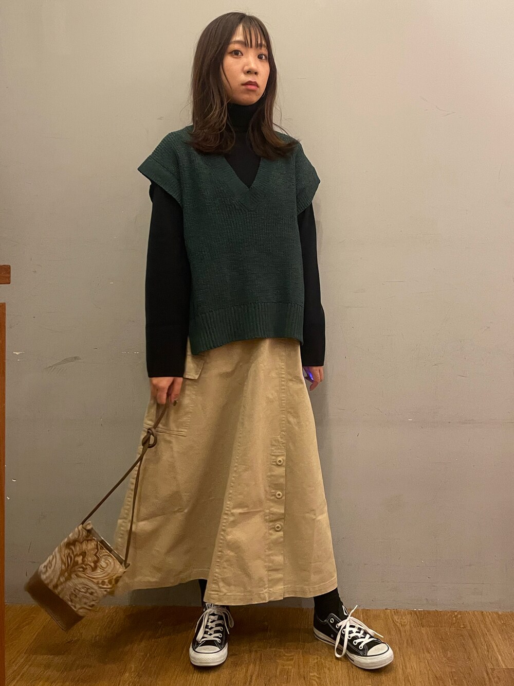 ベージュ系のスカート、グリーン系のベスト、ブラック系のニット/セーターを着用したレディースの冬コーディネートの2枚目の写真