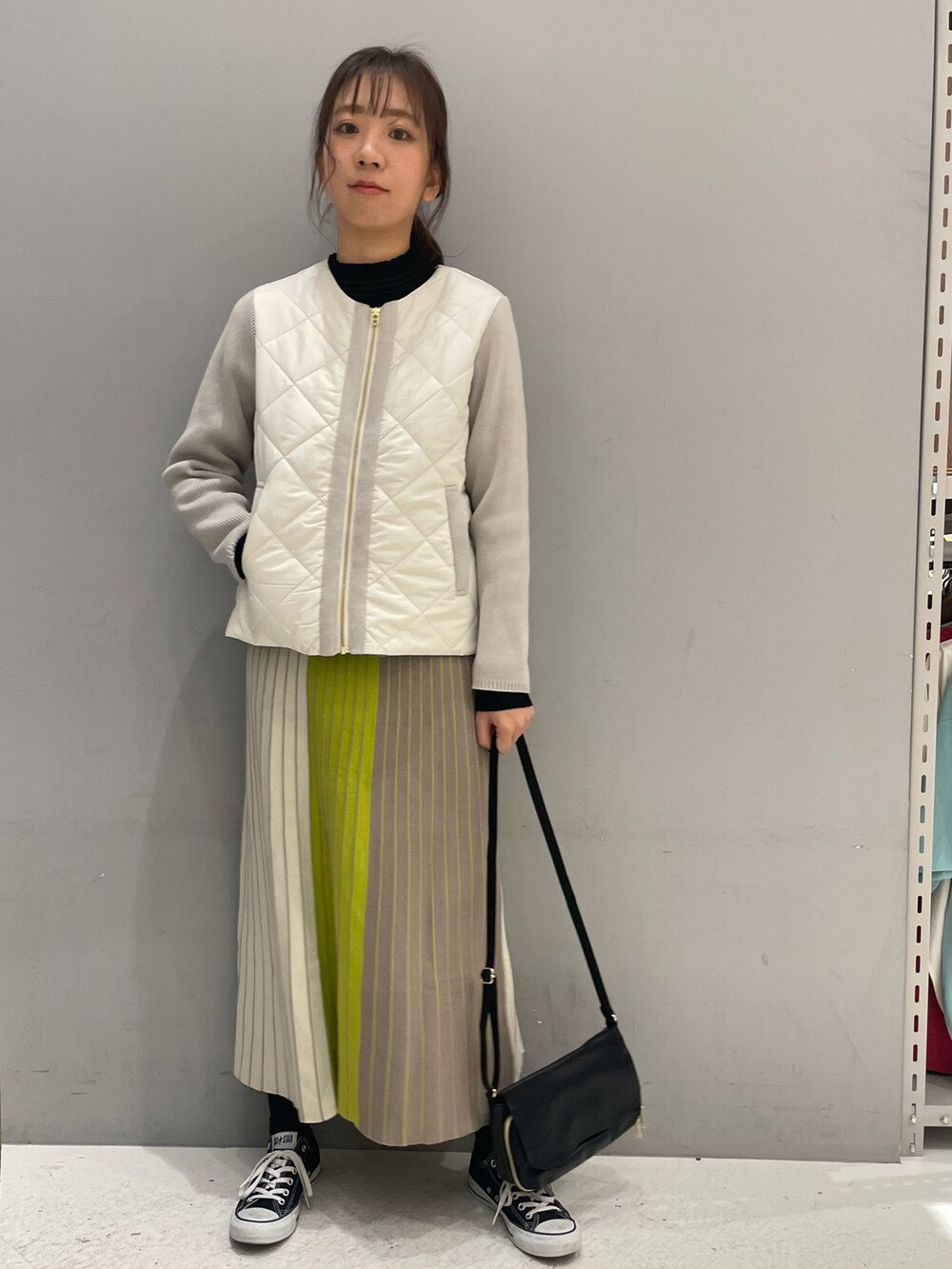 イエロー系のスカート、ホワイト系のブルゾン、ブラック系のニット/セーターを着用したレディースの冬コーディネートの2枚目の写真