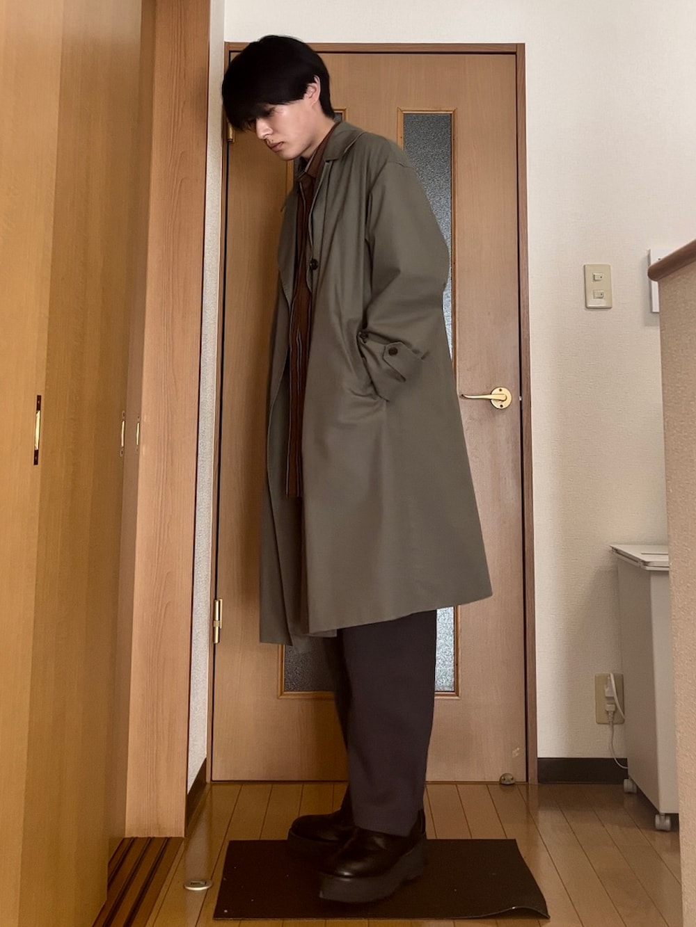 ブラック系のドレスシューズ、ブラウン系のシャツ/ブラウス、グリーン系のトレンチコートを着用したメンズの冬コーディネートの2枚目の写真