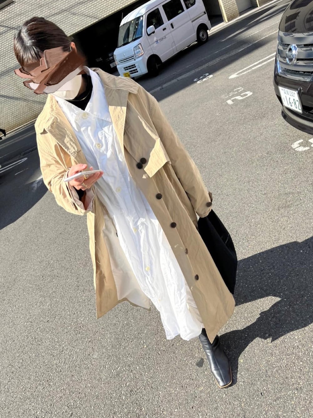 ベージュ系のトレンチコート、ホワイト系のワンピース、ブラック系のブーツを着用したレディースの冬コーディネートの2枚目の写真