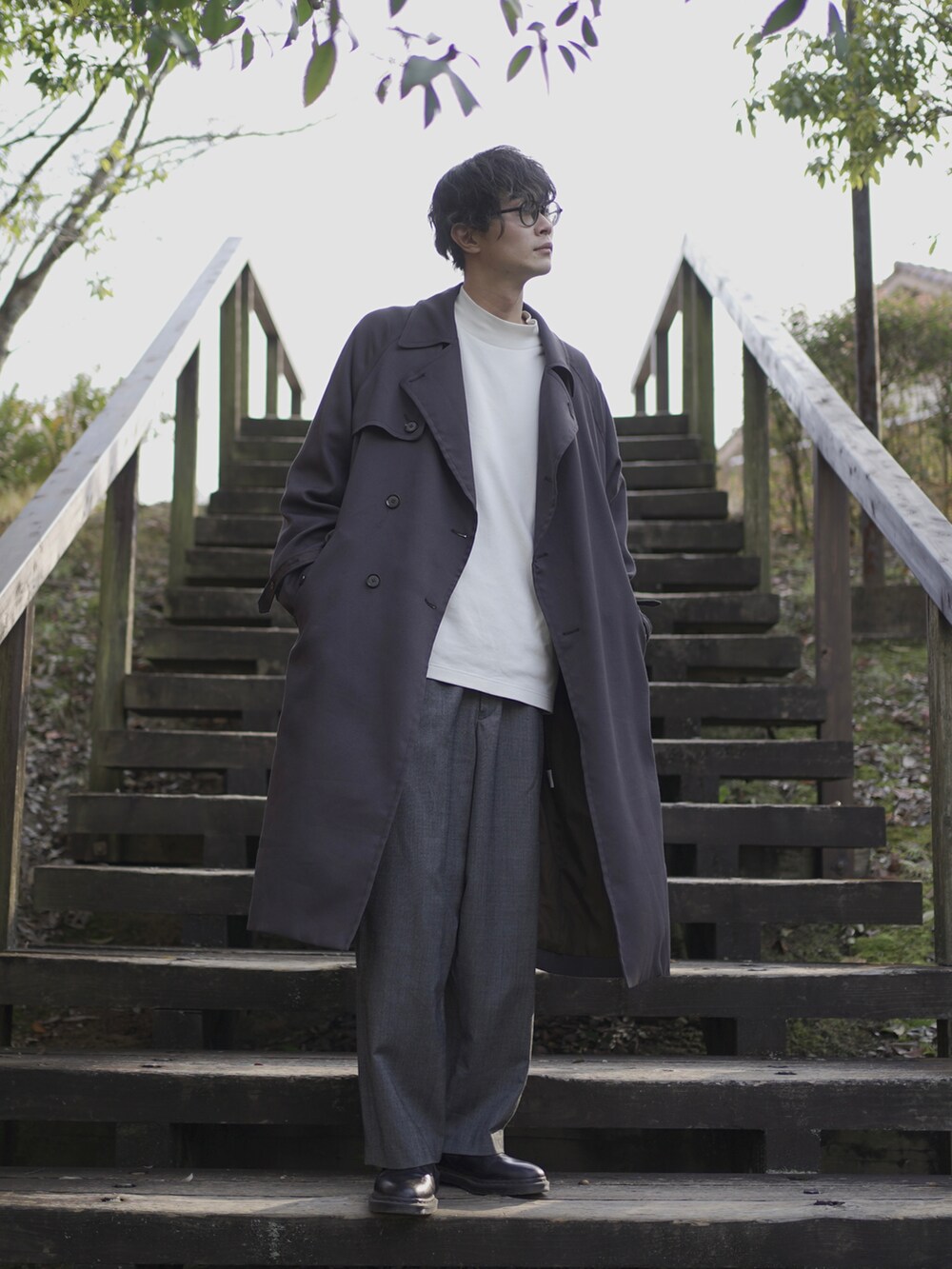 グレー系のトレンチコート、ホワイト系のTシャツ/カットソー、グレー系のスラックスを着用したメンズの冬コーディネートの2枚目の写真