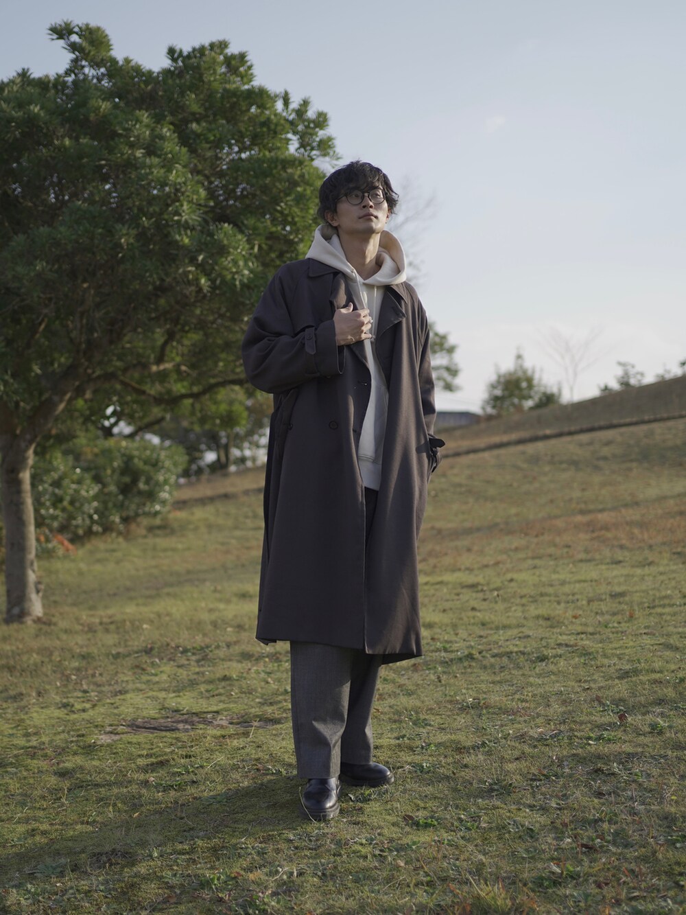 グレー系のトレンチコート、ホワイト系のパーカー、グレー系のスラックスを着用したメンズの冬コーディネートの3枚目の写真