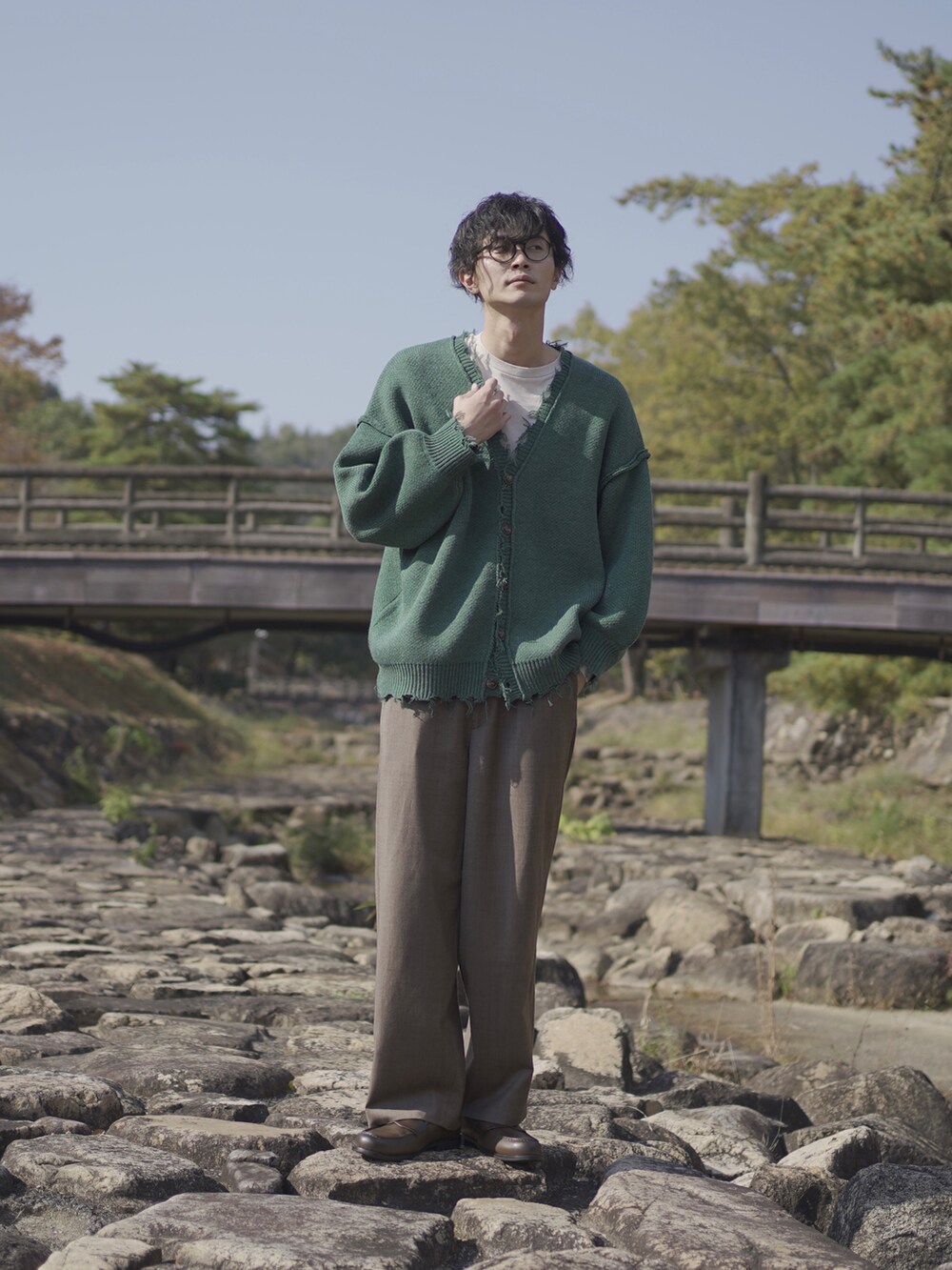 グリーン系のカーディガン/ボレロ、ベージュ系のTシャツ/カットソー、ブラウン系のスラックスを着用したメンズの秋コーディネートの2枚目の写真