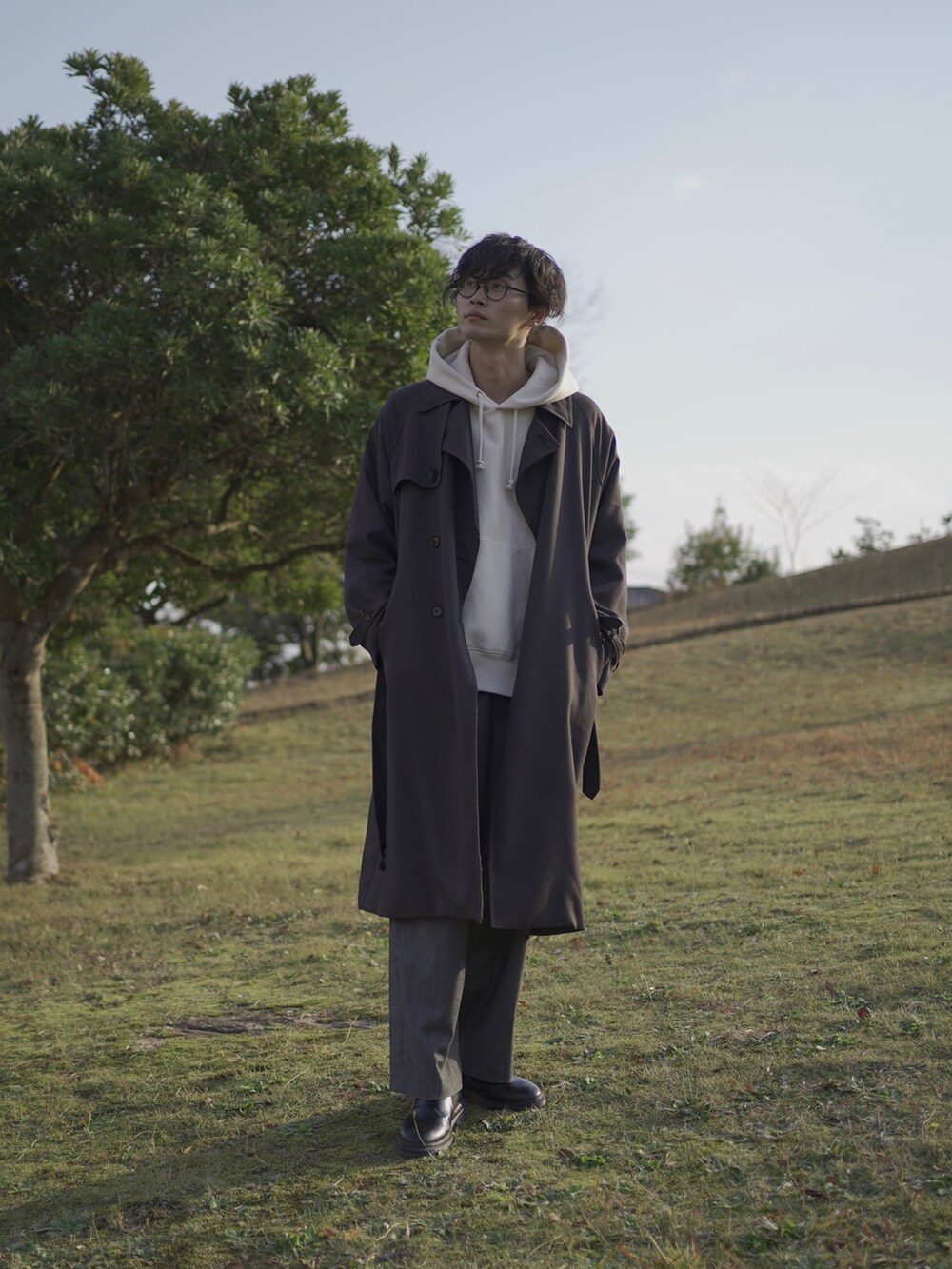 グレー系のトレンチコート、ホワイト系のパーカー、グレー系のスラックスを着用したメンズの冬コーディネートの2枚目の写真