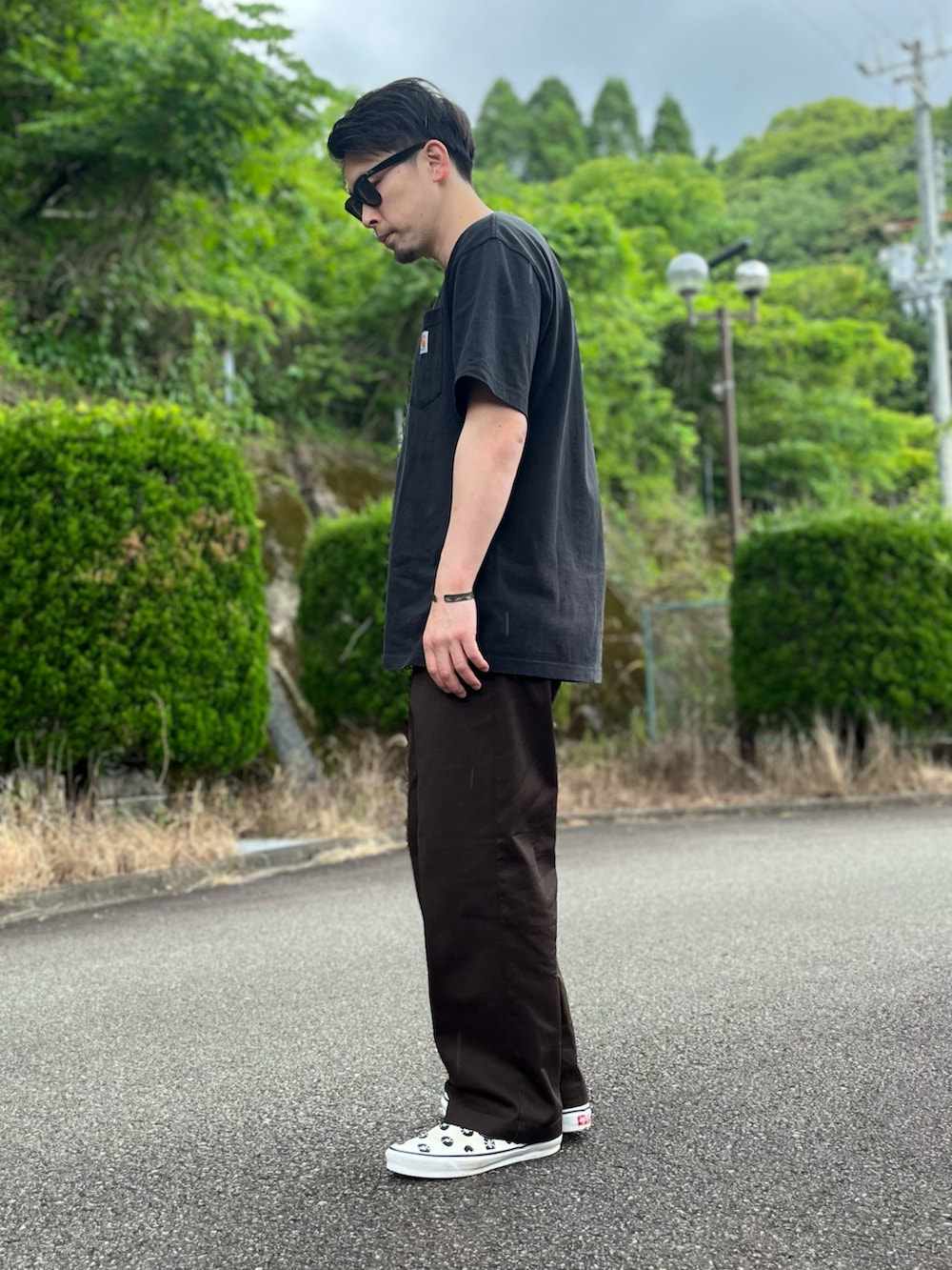 ブラック系のTシャツ/カットソー、ブラウン系のチノパンツ、ホワイト系のスリッポンを着用したメンズの春コーディネートの2枚目の写真