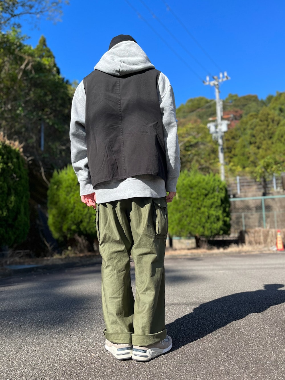 グレー系のパーカー、ブラック系のベスト、グリーン系のカーゴパンツを着用したメンズの秋コーディネートの3枚目の写真