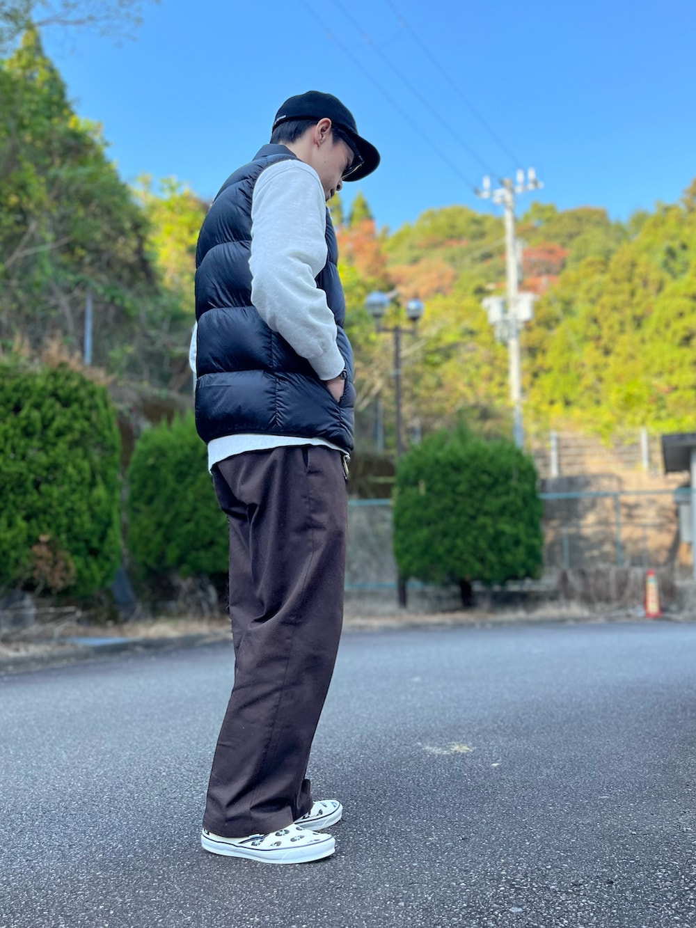 グレー系のスウェット、ブラック系のダウンベスト、ブラウン系のチノパンツを着用したメンズの秋コーディネートの2枚目の写真