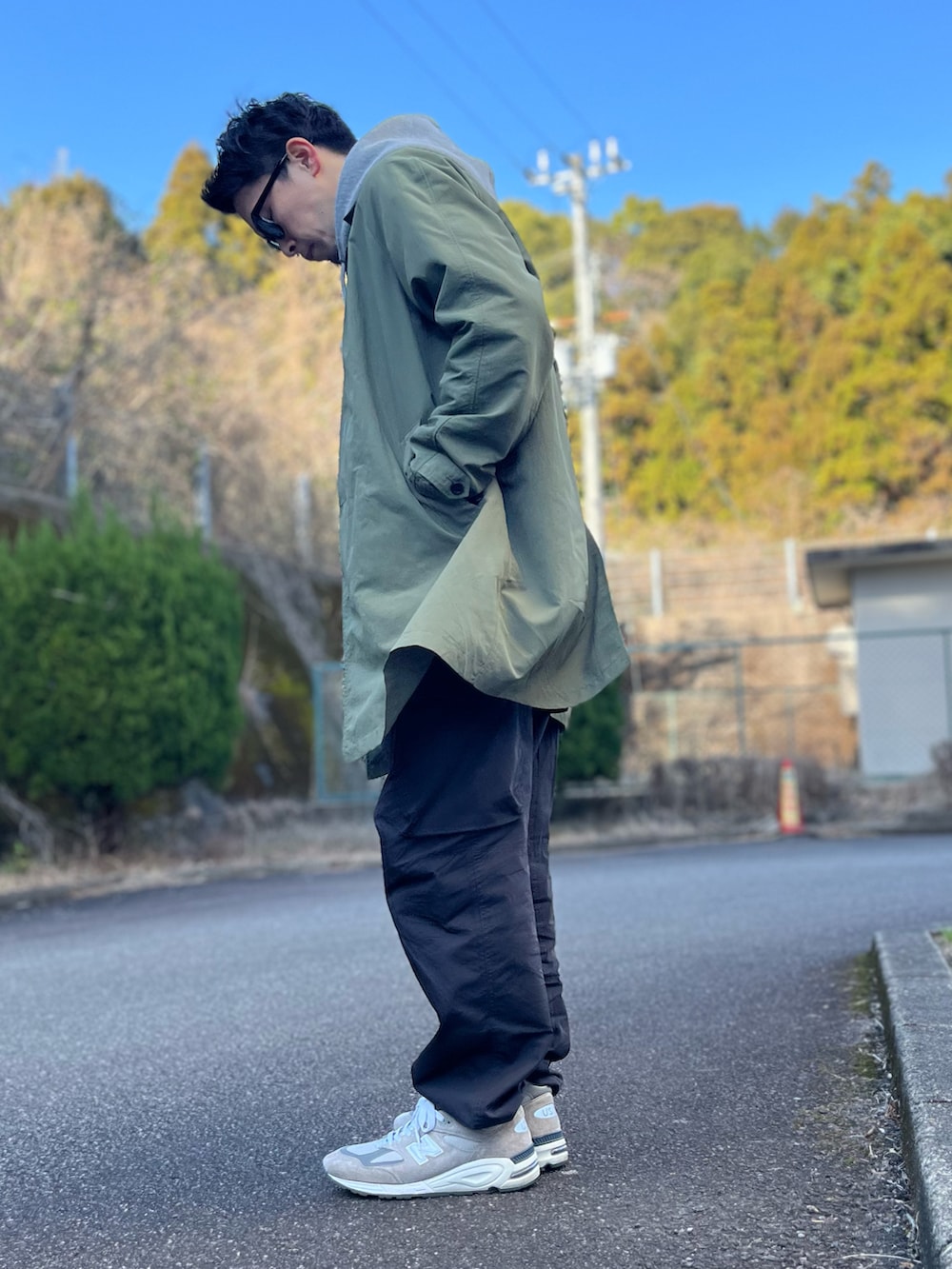 グレー系のパーカー、グリーン系のステンカラーコート、ブラック系のパンツを着用したメンズの冬コーディネートの4枚目の写真