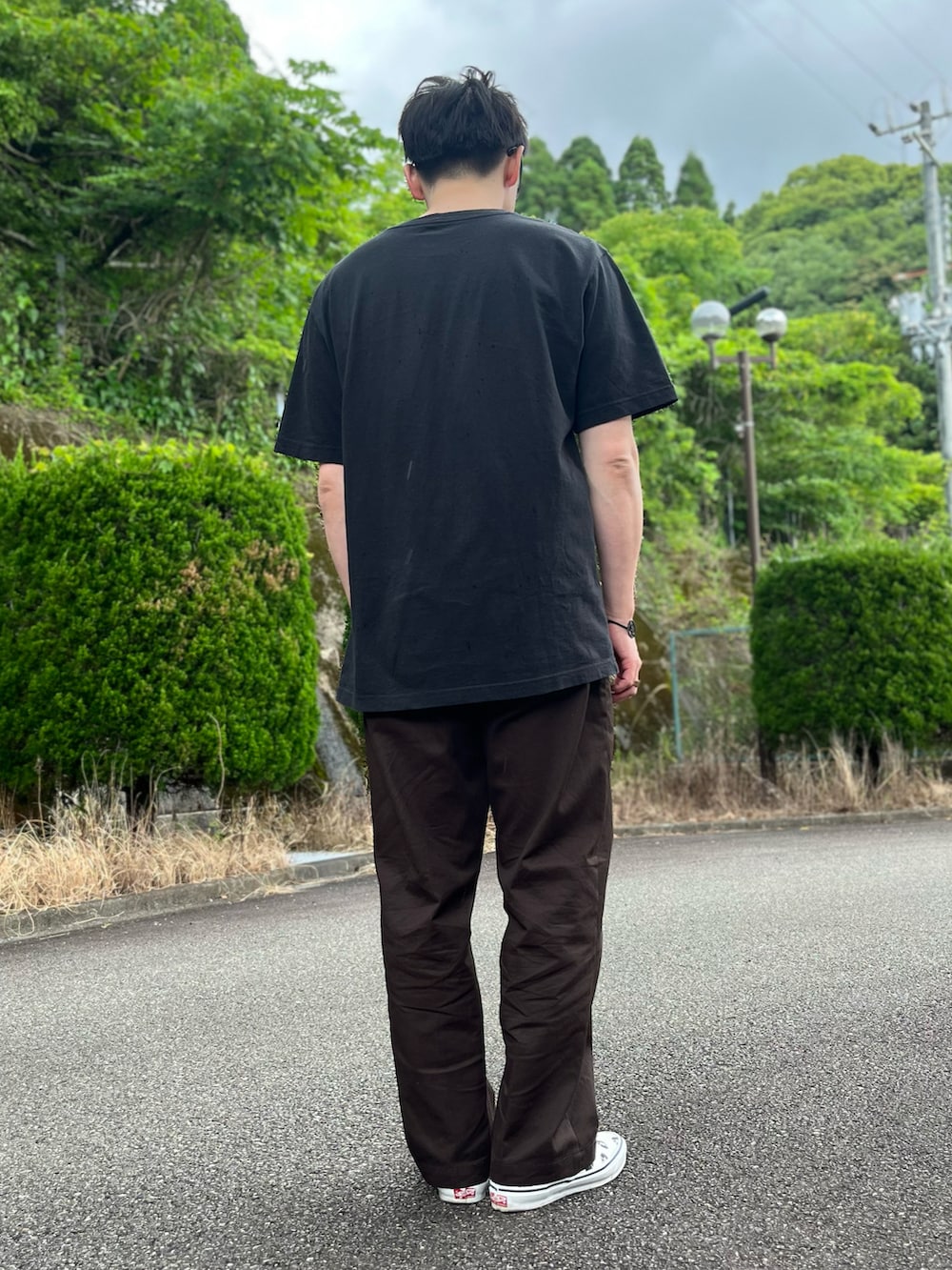 ブラック系のTシャツ/カットソー、ブラウン系のチノパンツ、ホワイト系のスリッポンを着用したメンズの春コーディネートの3枚目の写真