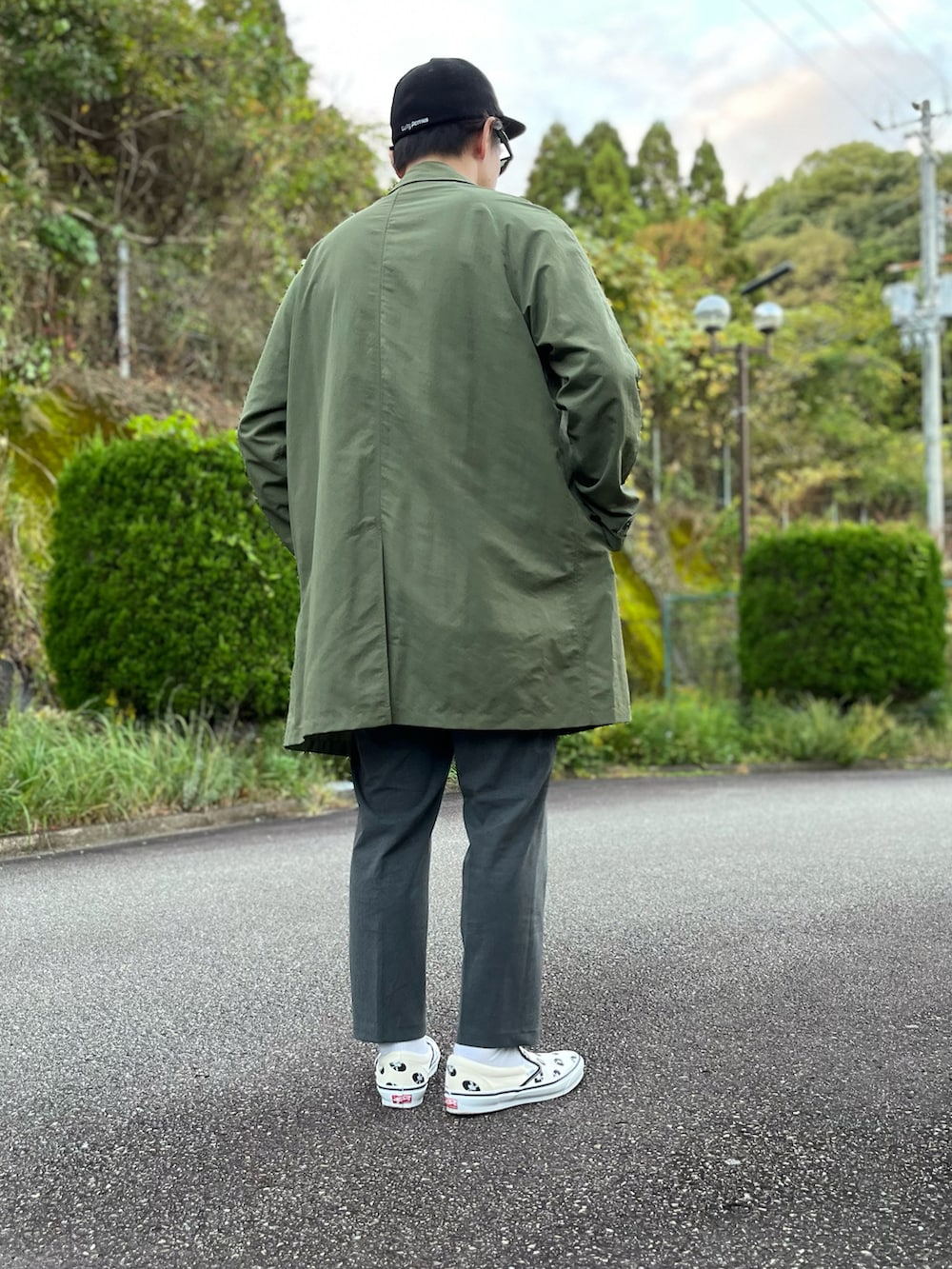 グリーン系のステンカラーコート、ホワイト系のTシャツ/カットソー、グレー系のその他パンツを着用したメンズの秋コーディネートの2枚目の写真