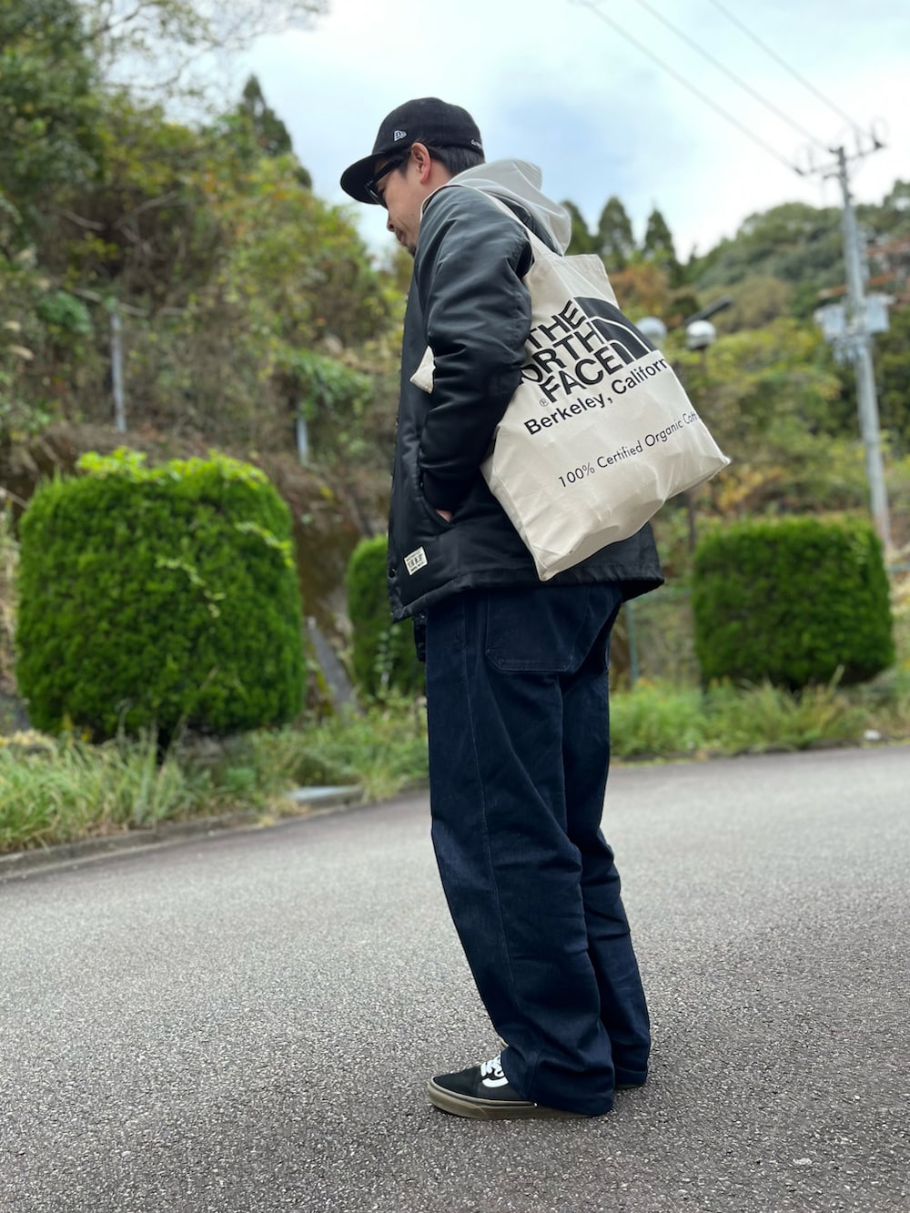 ホワイト系のパーカー、ホワイト系のトートバッグ、ブラック系のナイロンジャケットを着用したメンズの秋コーディネートの2枚目の写真