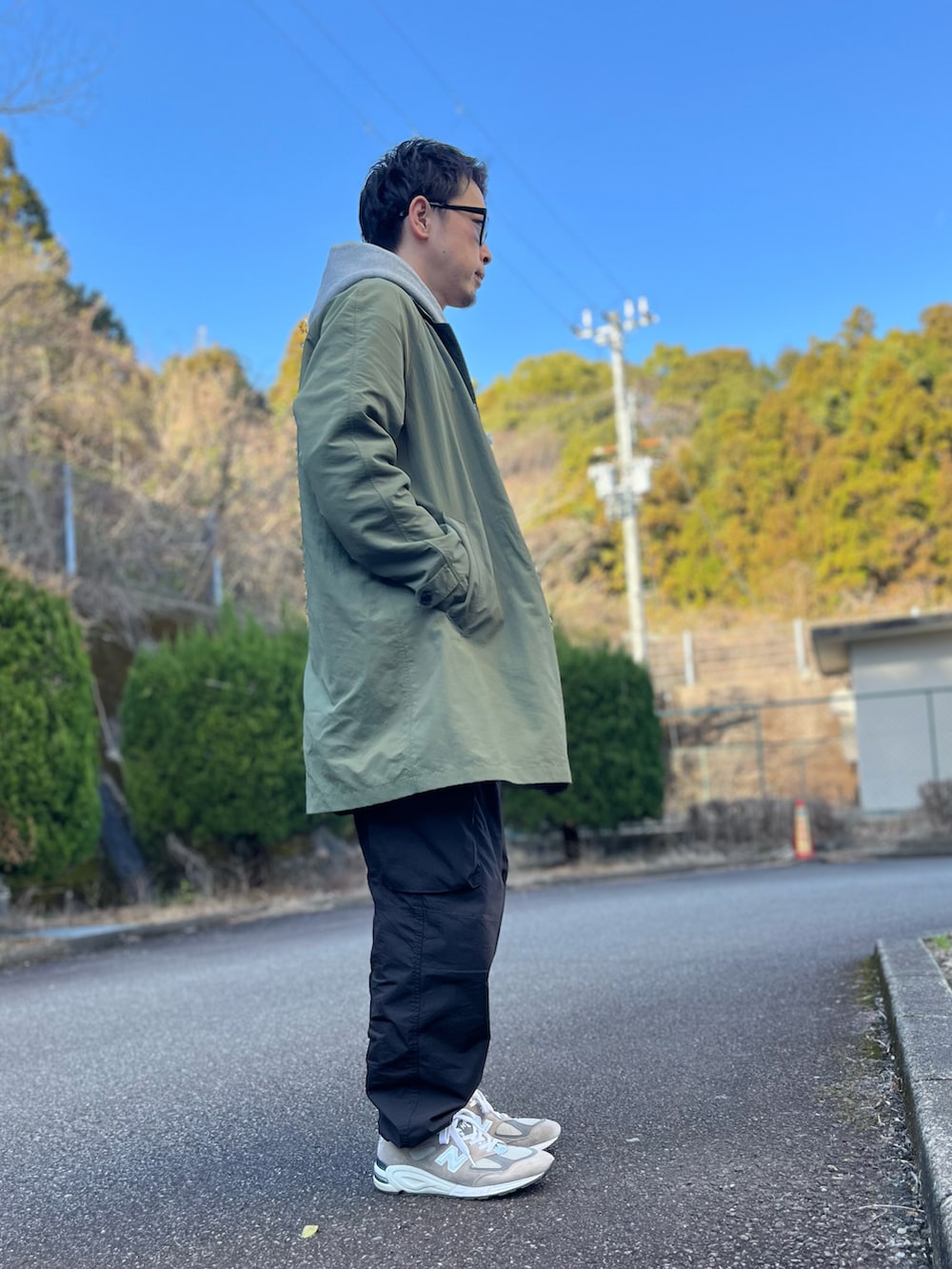 グレー系のパーカー、グリーン系のステンカラーコート、ブラック系のパンツを着用したメンズの冬コーディネートの2枚目の写真