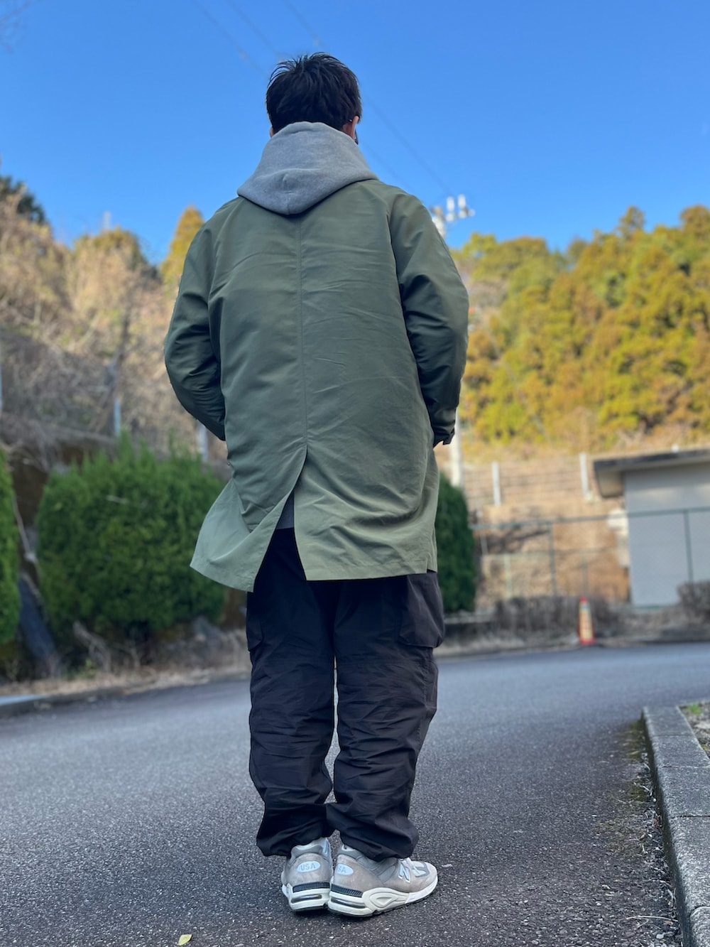 グレー系のパーカー、グリーン系のステンカラーコート、ブラック系のパンツを着用したメンズの冬コーディネートの3枚目の写真