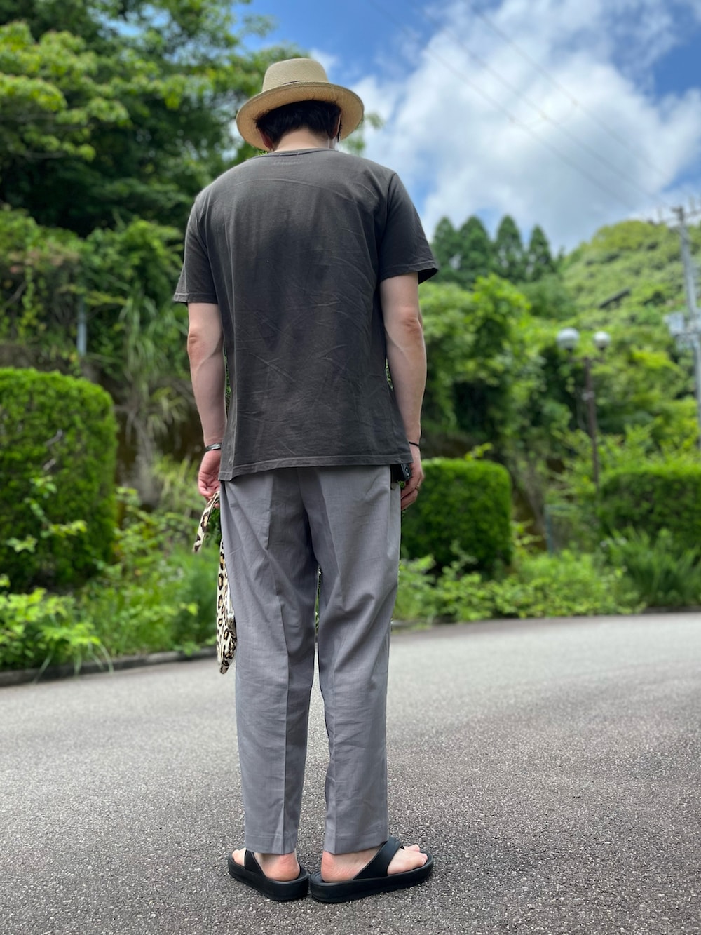 ブラック系のTシャツ/カットソー、その他のクラッチバッグ、グレー系のパンツを着用したメンズの夏コーディネートの4枚目の写真