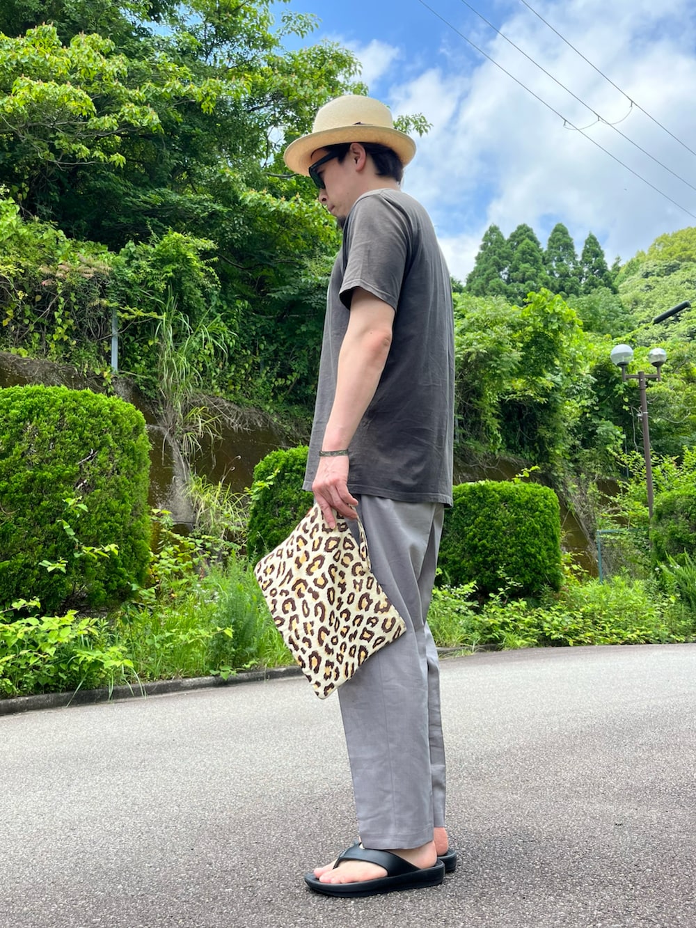 ブラック系のTシャツ/カットソー、その他のクラッチバッグ、グレー系のパンツを着用したメンズの夏コーディネートの3枚目の写真