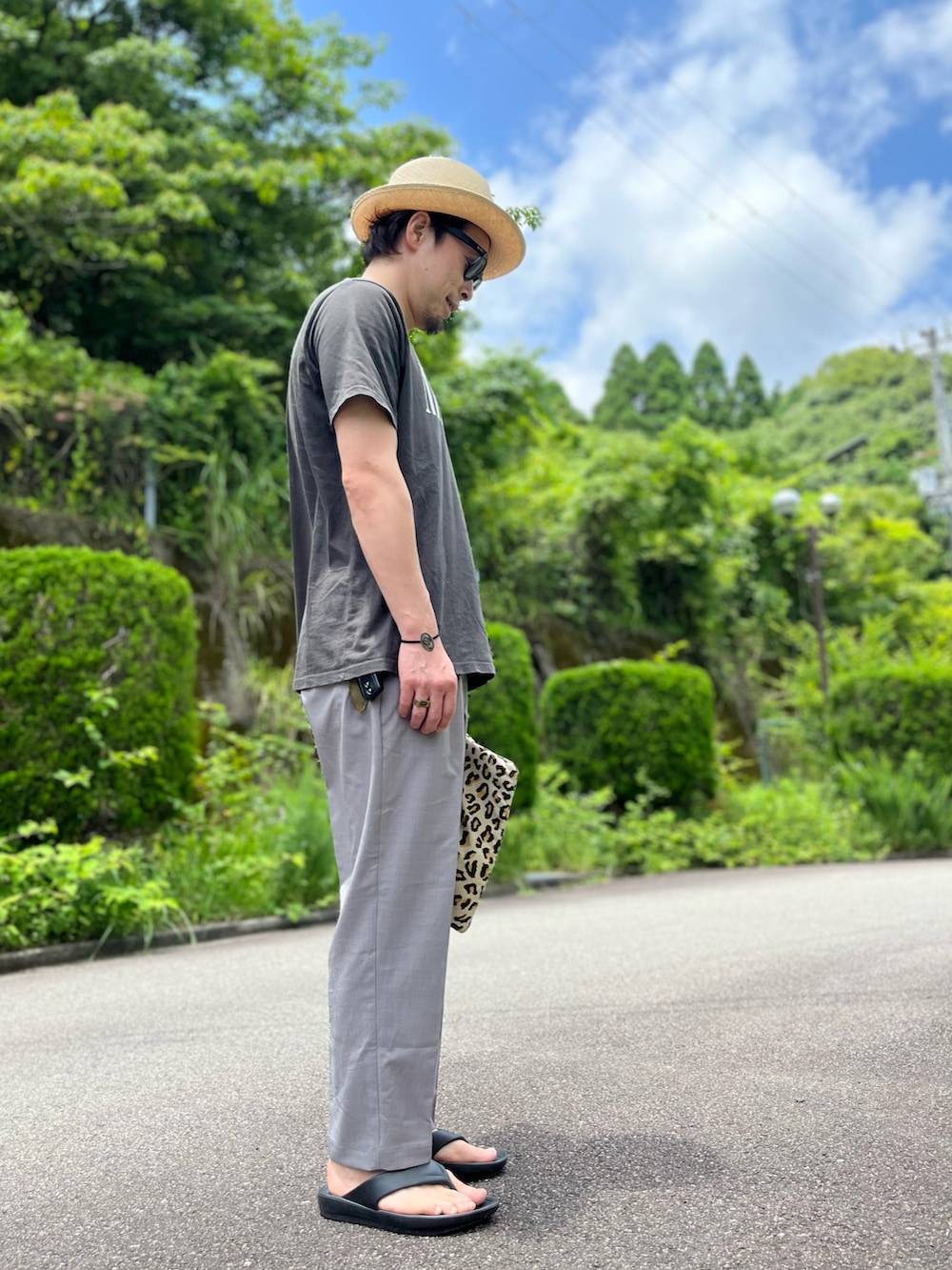 ブラック系のTシャツ/カットソー、その他のクラッチバッグ、グレー系のパンツを着用したメンズの夏コーディネートの2枚目の写真