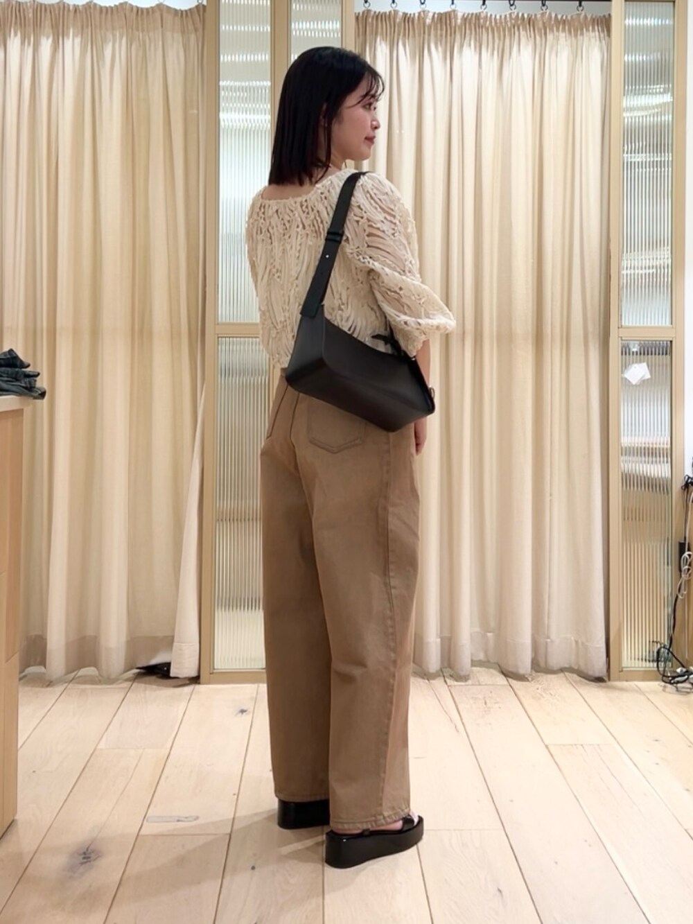 ベージュ系のトップス、ブルー系のデニムパンツ、ブラック系のサンダルを着用したレディースの春コーディネートの2枚目の写真