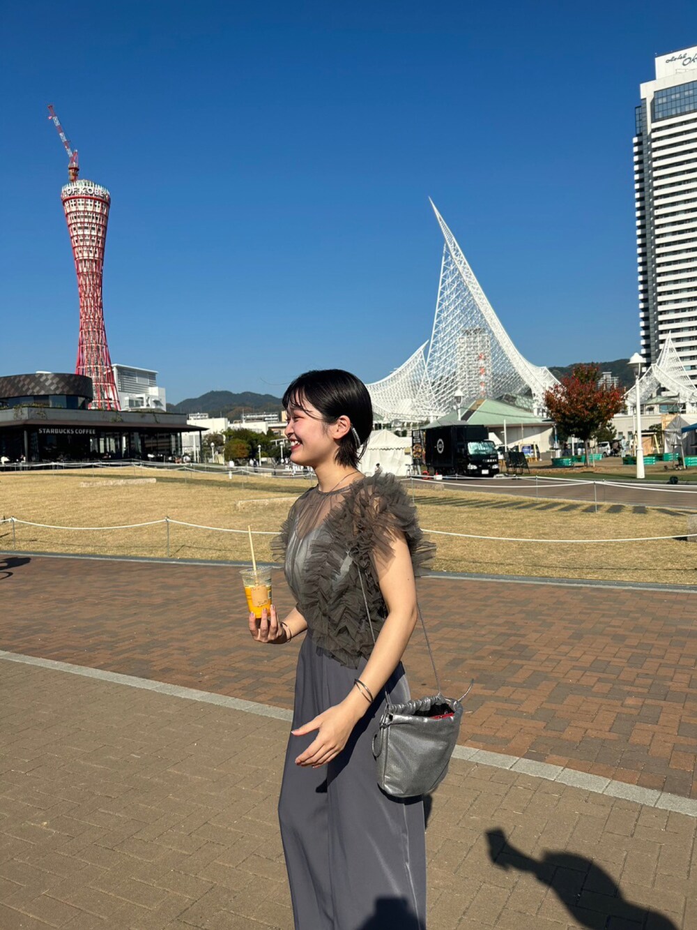 グレー系のパンツドレス、ブラック系のパンプス、ゴールド系のショルダーバッグを着用したレディースの秋コーディネートの3枚目の写真