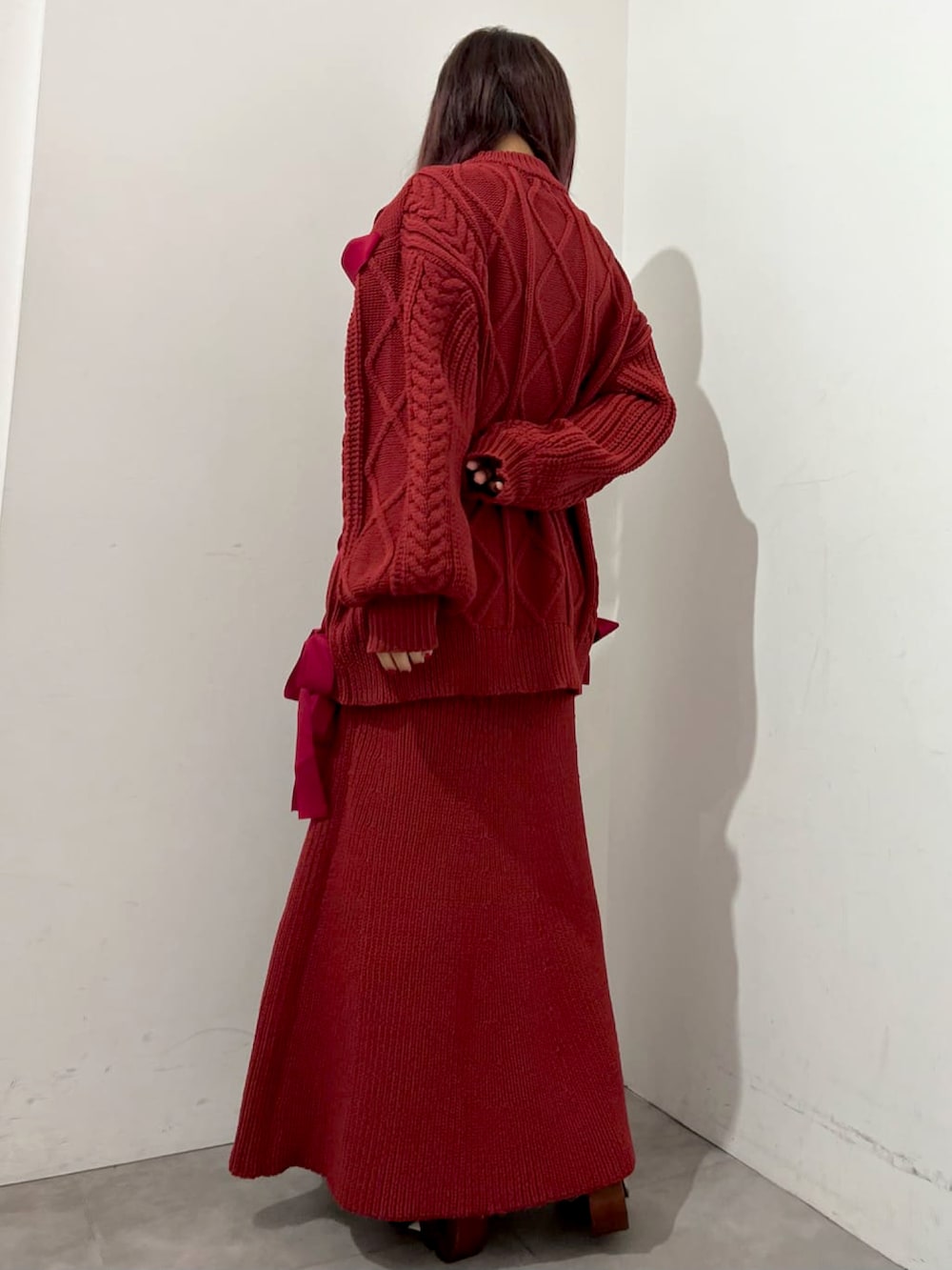 レッド系のニット/セーター、レッド系のスカート、ベージュ系のブーツを着用したレディースの秋コーディネートの2枚目の写真