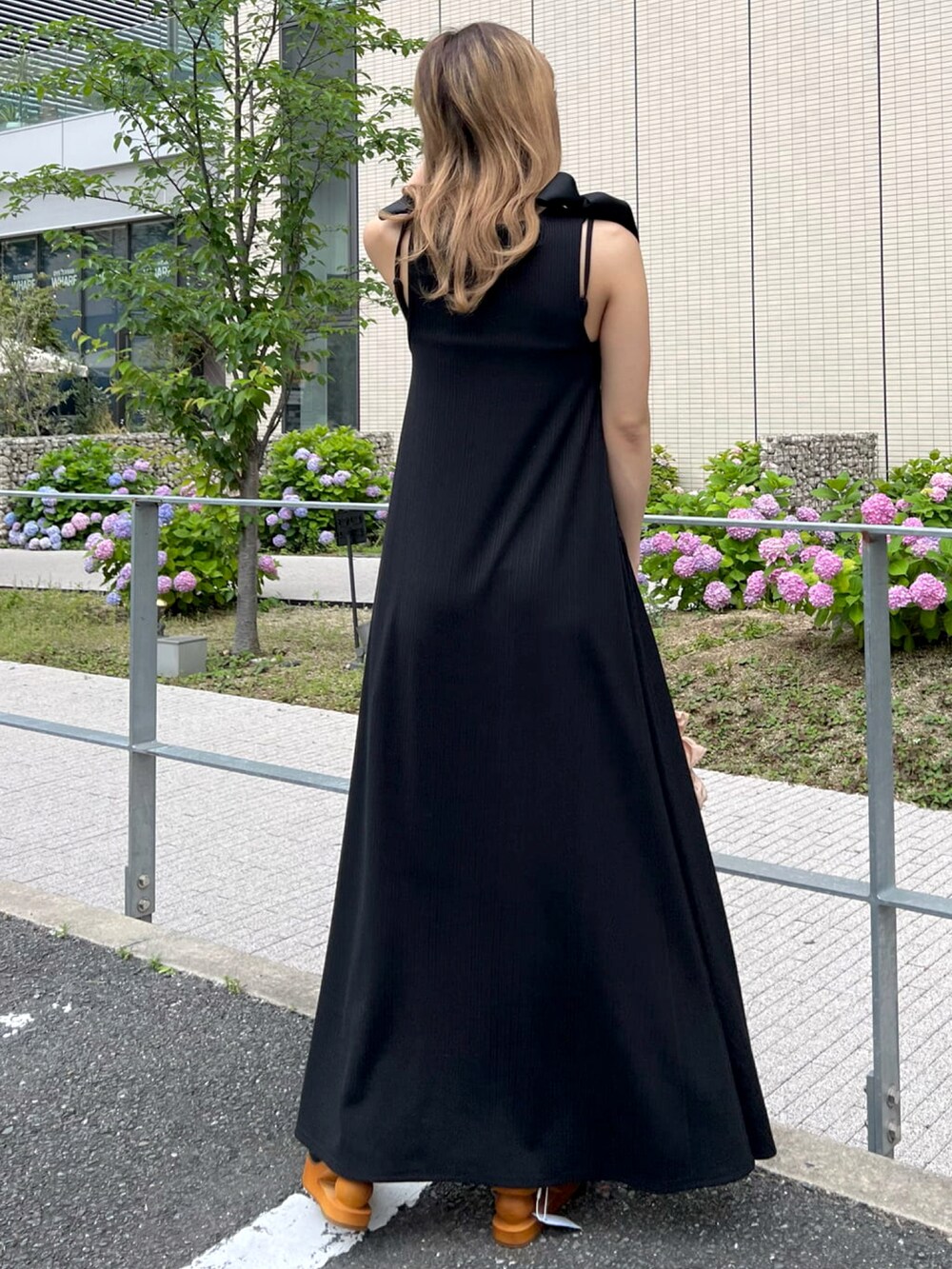 ブラック系のワンピース、ブラック系のサンダル、オレンジ系のハンドバッグを着用したレディースの夏コーディネートの2枚目の写真