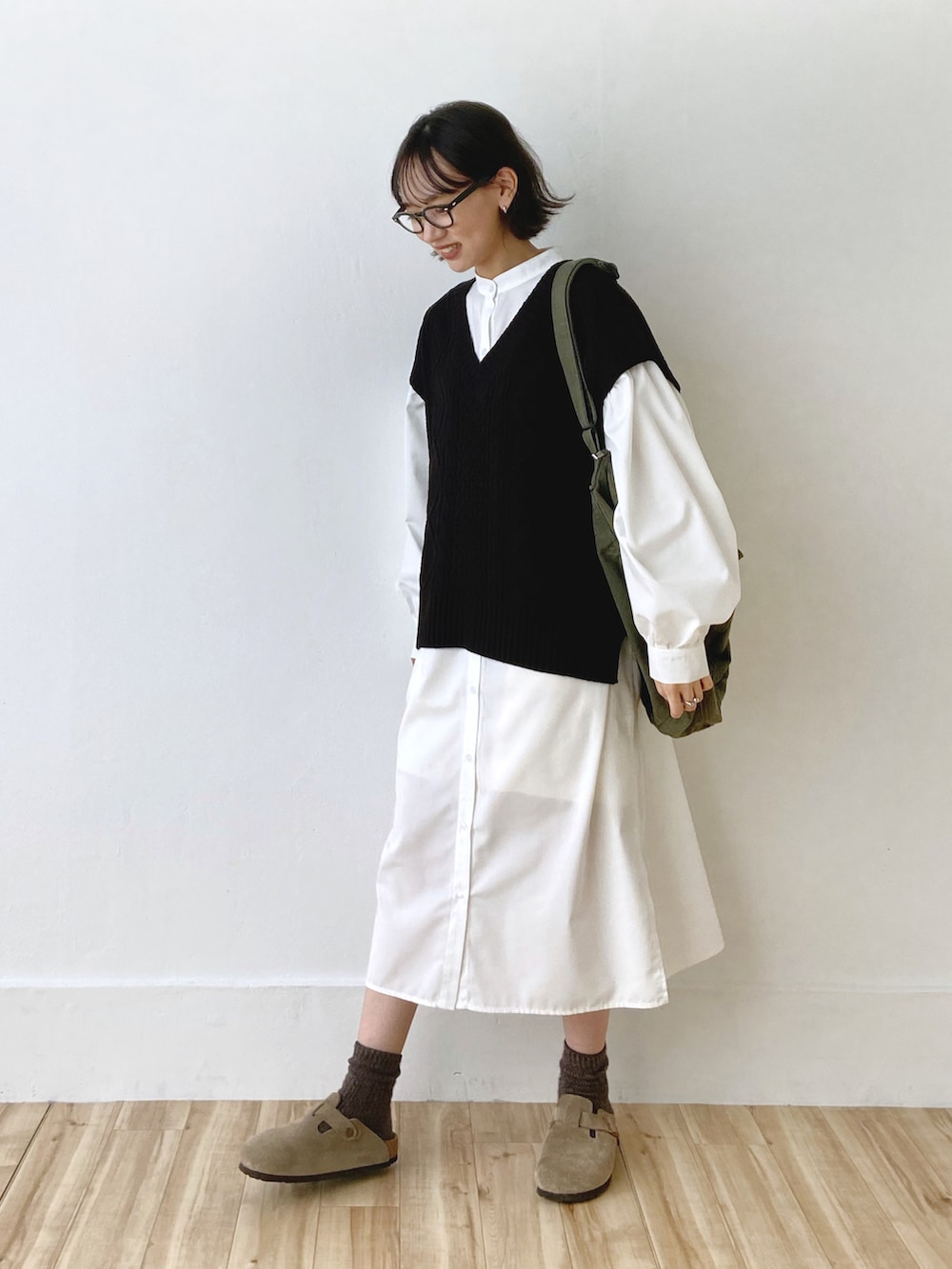 ホワイト系のシャツワンピース、ブラック系のベスト、グリーン系のショルダーバッグを着用したレディースの秋コーディネートの2枚目の写真