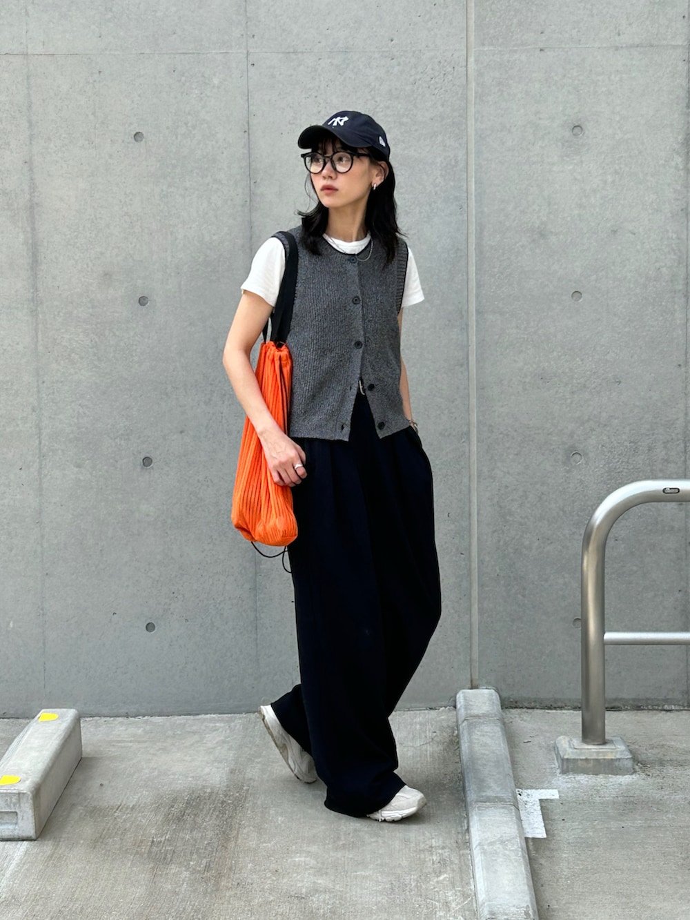 ブラック系のその他パンツ、ブラック系のベスト、オレンジ系のトートバッグを着用したレディースの春コーディネートの2枚目の写真