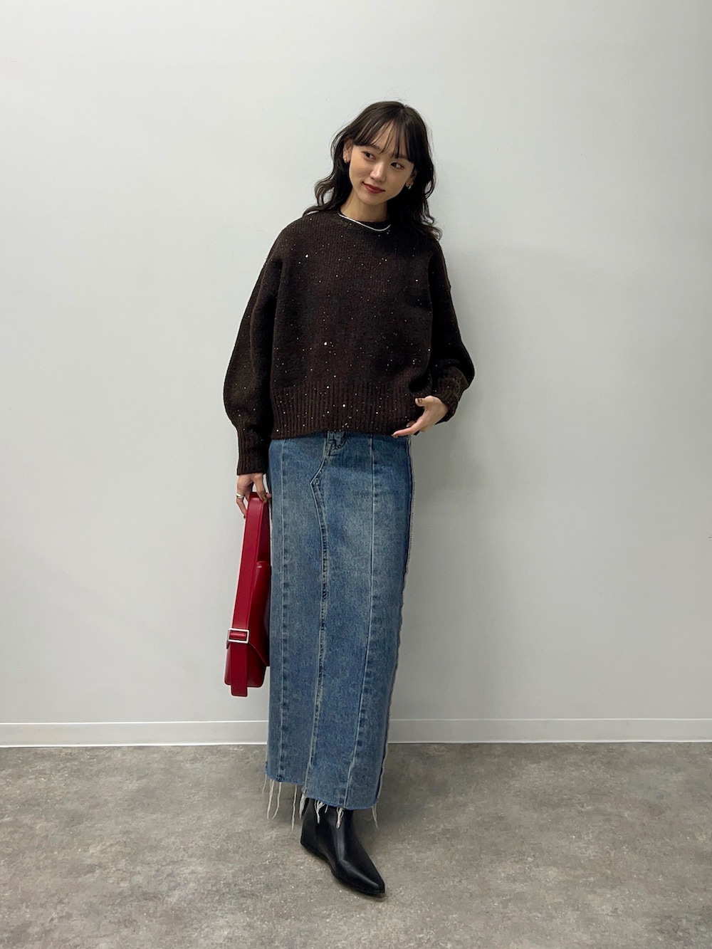 ブラウン系のニット/セーター、ブルー系のデニムスカート、レッド系のショルダーバッグを着用したレディースの秋コーディネートの2枚目の写真