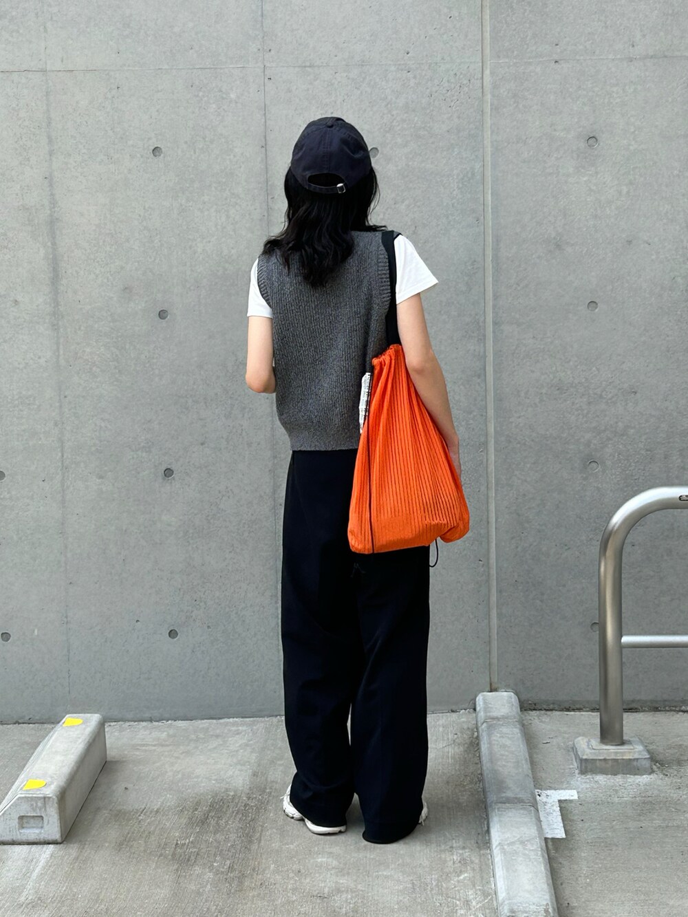 ブラック系のその他パンツ、ブラック系のベスト、オレンジ系のトートバッグを着用したレディースの春コーディネートの4枚目の写真