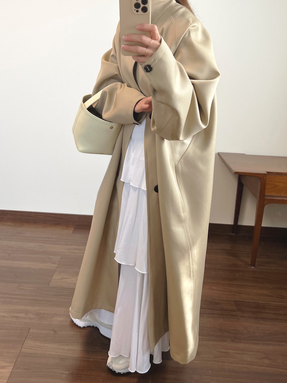 ベージュ系のステンカラーコート、ホワイト系のスカート、ホワイト系のスニーカーを着用したレディースの春コーディネートの2枚目の写真