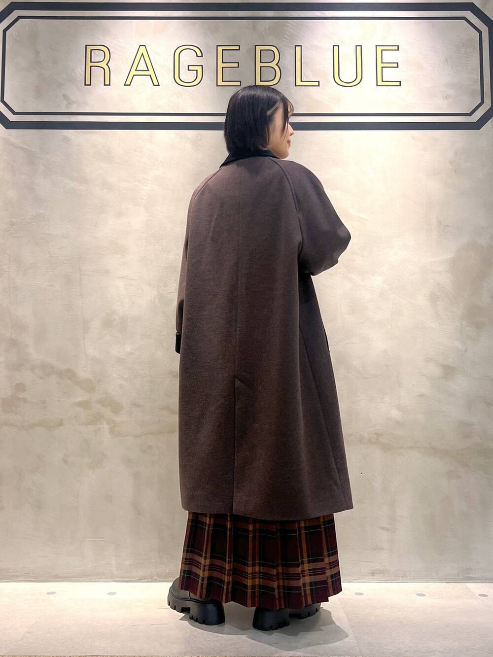 ブラウン系のステンカラーコート、レッド系のスカート、ブラック系のブーツを着用したレディースの秋コーディネートの7枚目の写真