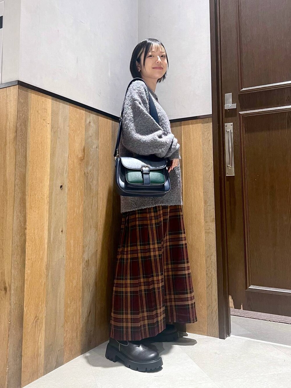 グリーン系のニット/セーター、ブラック系のブーツ、ブルー系のショルダーバッグを着用したレディースの秋コーディネートの2枚目の写真