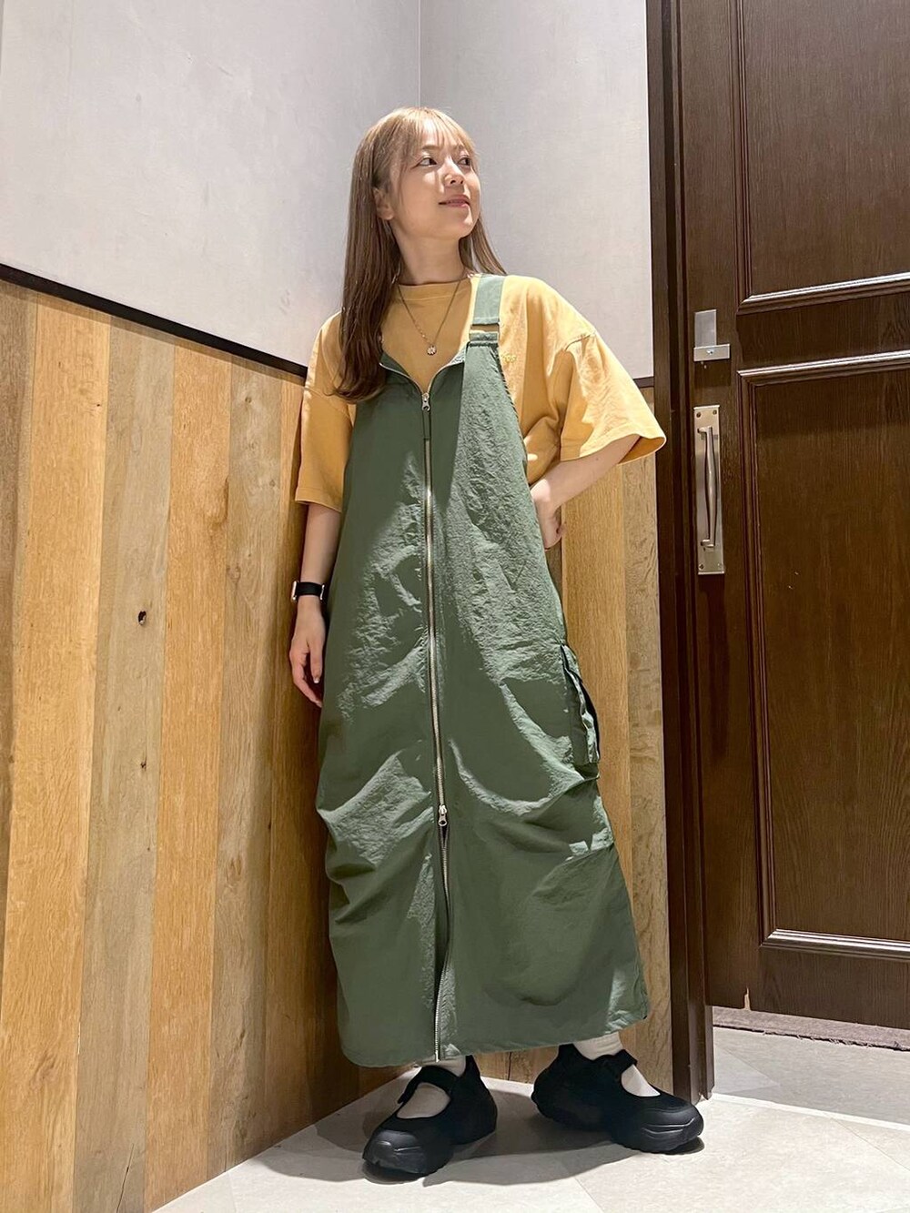 グリーン系のジャンパースカート、ブラック系のスニーカー、イエロー系のTシャツ/カットソーを着用したレディースの夏コーディネートの5枚目の写真